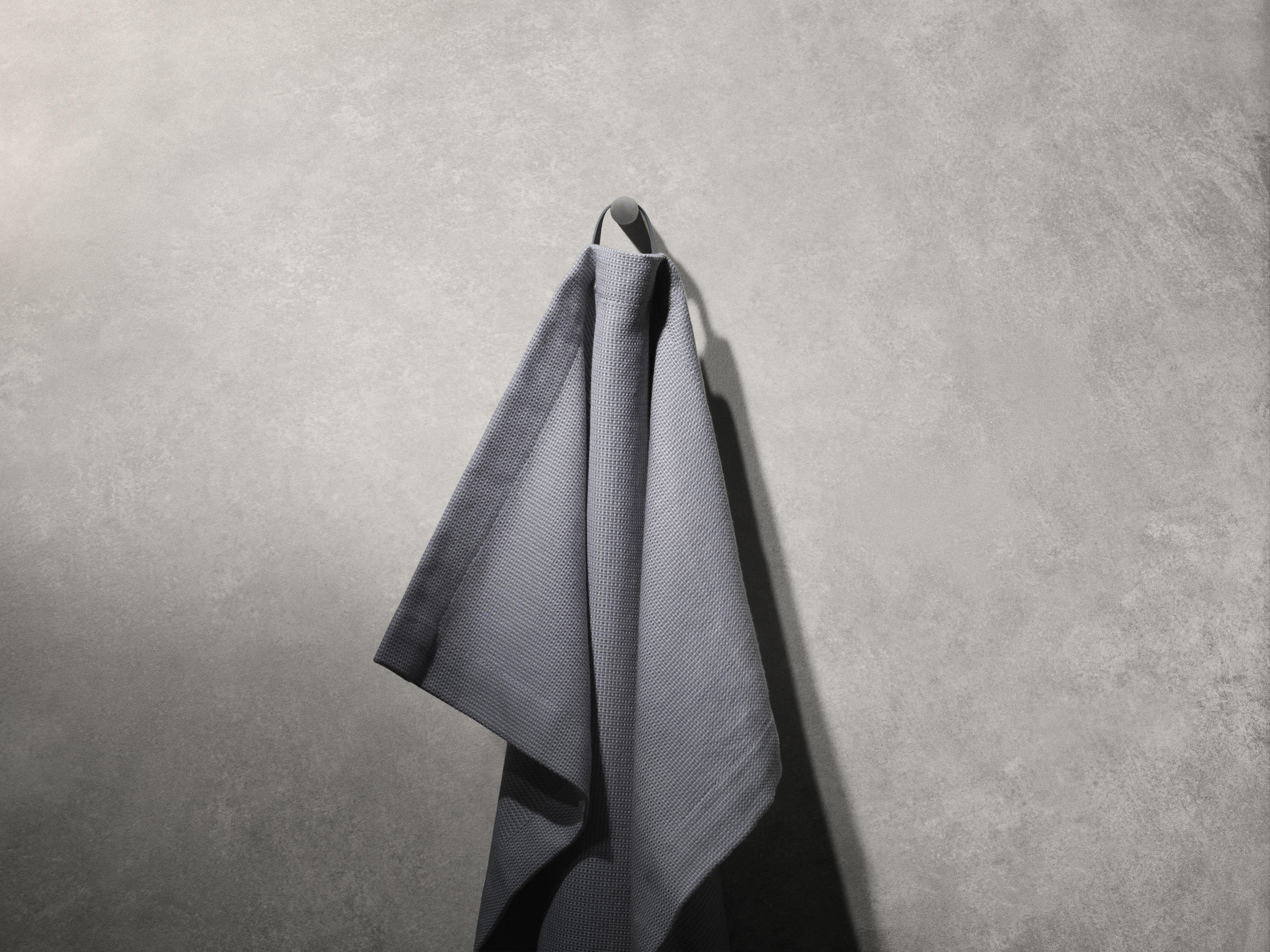 Graues Handtuch hängt an einem Vipp Handtuchhaken. Badezimmer Accessoires für moderne Badezimmer.