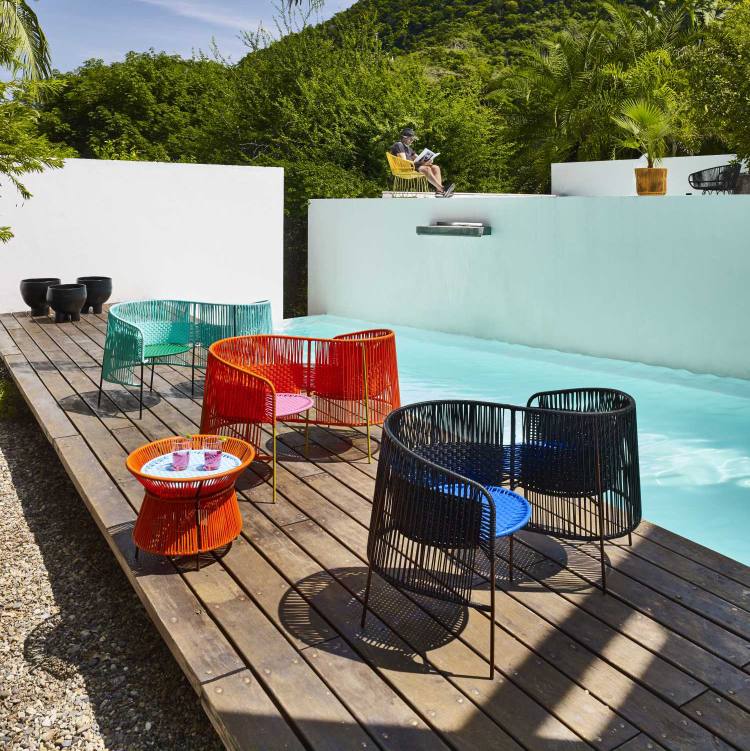 Caribe Beistelltisch niedrig in Orange, Kaugummirosa und Currygelb neben Pool mit bunten Outdoor-Stühlen.