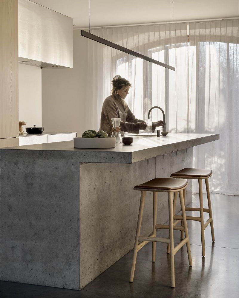 Osso Barhocker von Ethnicraft in moderner Küche mit Betoninsel und braunem Sitzpolster.