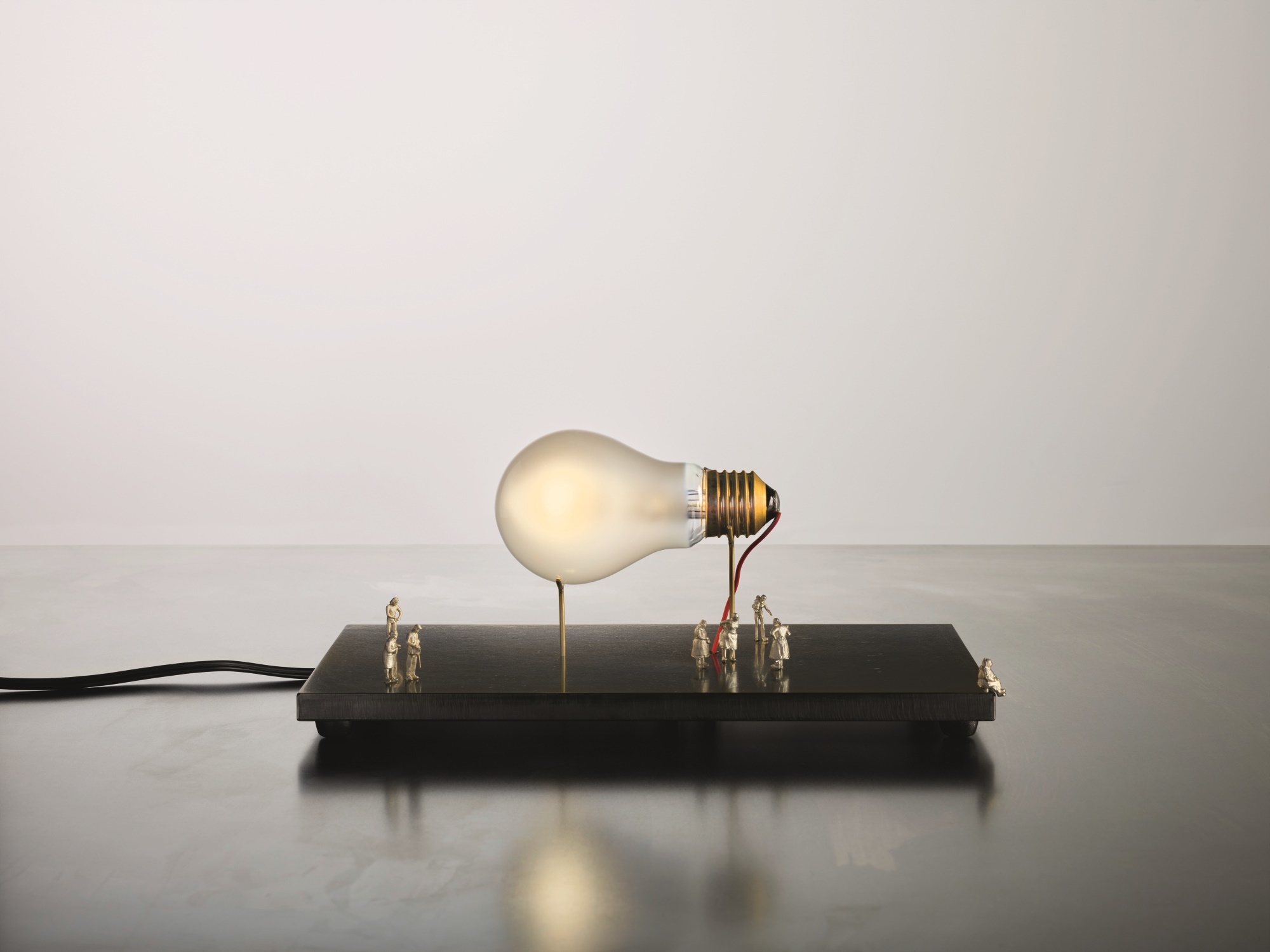 I Ricchi Poveri Tischleuchte: Glühbirne auf Sockel mit kleinen Figuren. Designlampe von Ingo Maurer.