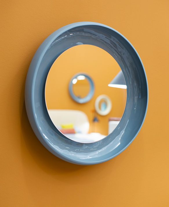 Blauer Coque Spiegel von Miniforms mit Keramikrahmen an ockerfarbener Wand. Runder Wandspiegel.