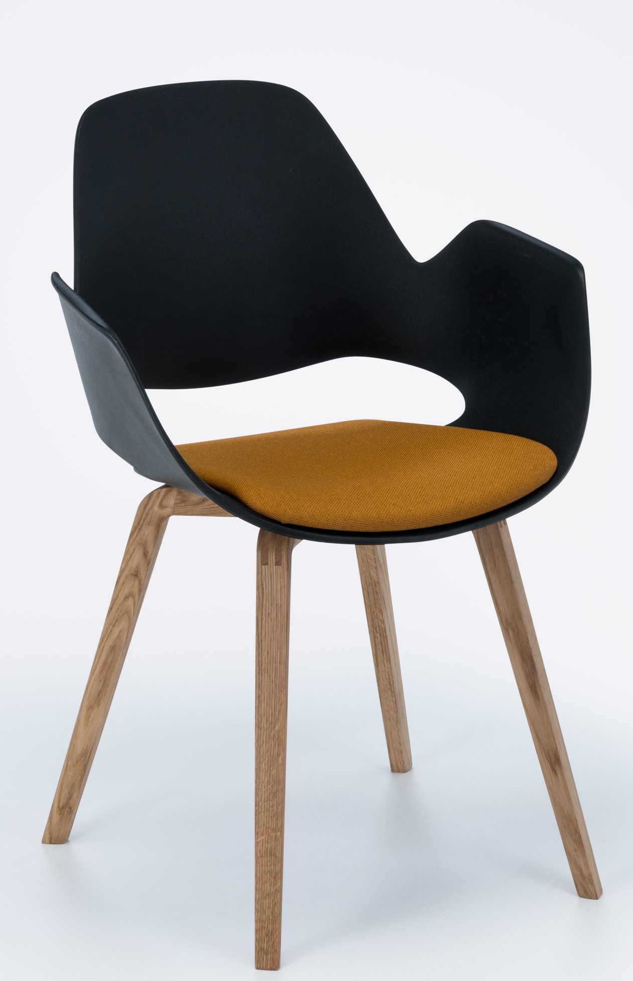 Falk Stuhl mit Armlehne von Houe: Schwarze Sitzschale, gelbes Kissen und Eichenholzbeine.