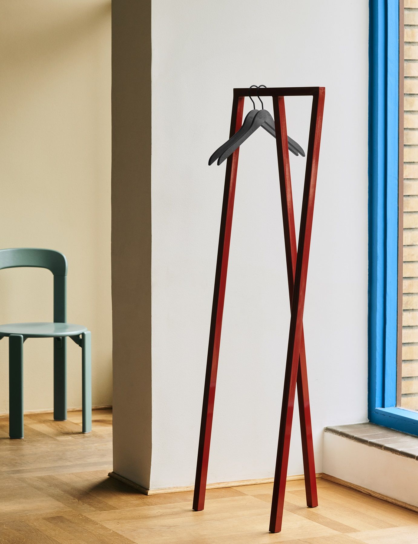 Rote Hay Loop Stand Hall Garderobe mit Kleiderbügeln vor weißer Wand und blauem Fenster.