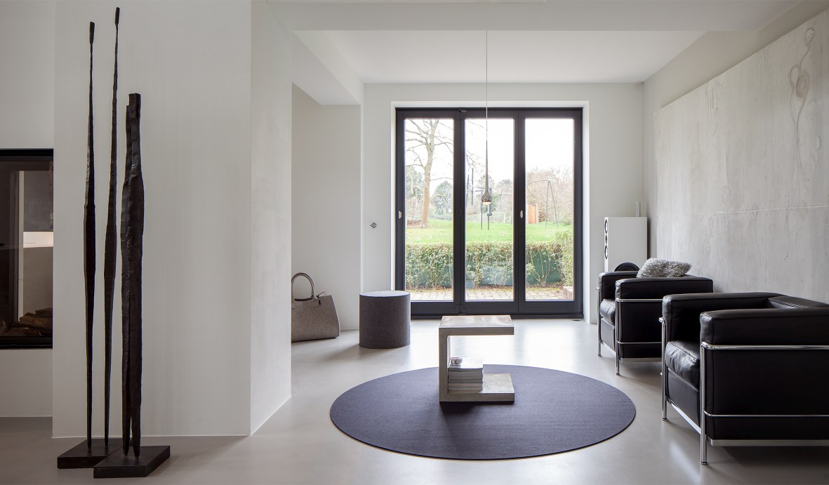 Moderner Wohnraum mit rundem, anthrazitfarbenem Teppich Bigdot von Hey Sign unter einem Beton-Couchtisch.