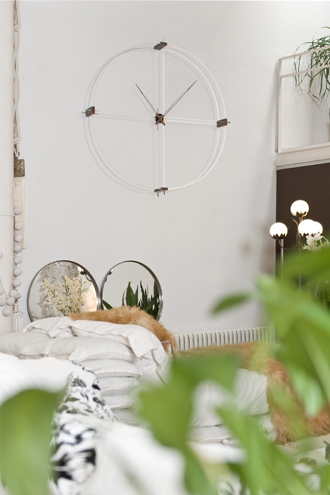 Delmori Clock Wanduhr in Weiß/Chrom an einer weißen Wand über einem Bett. Moderne Wanddekoration.