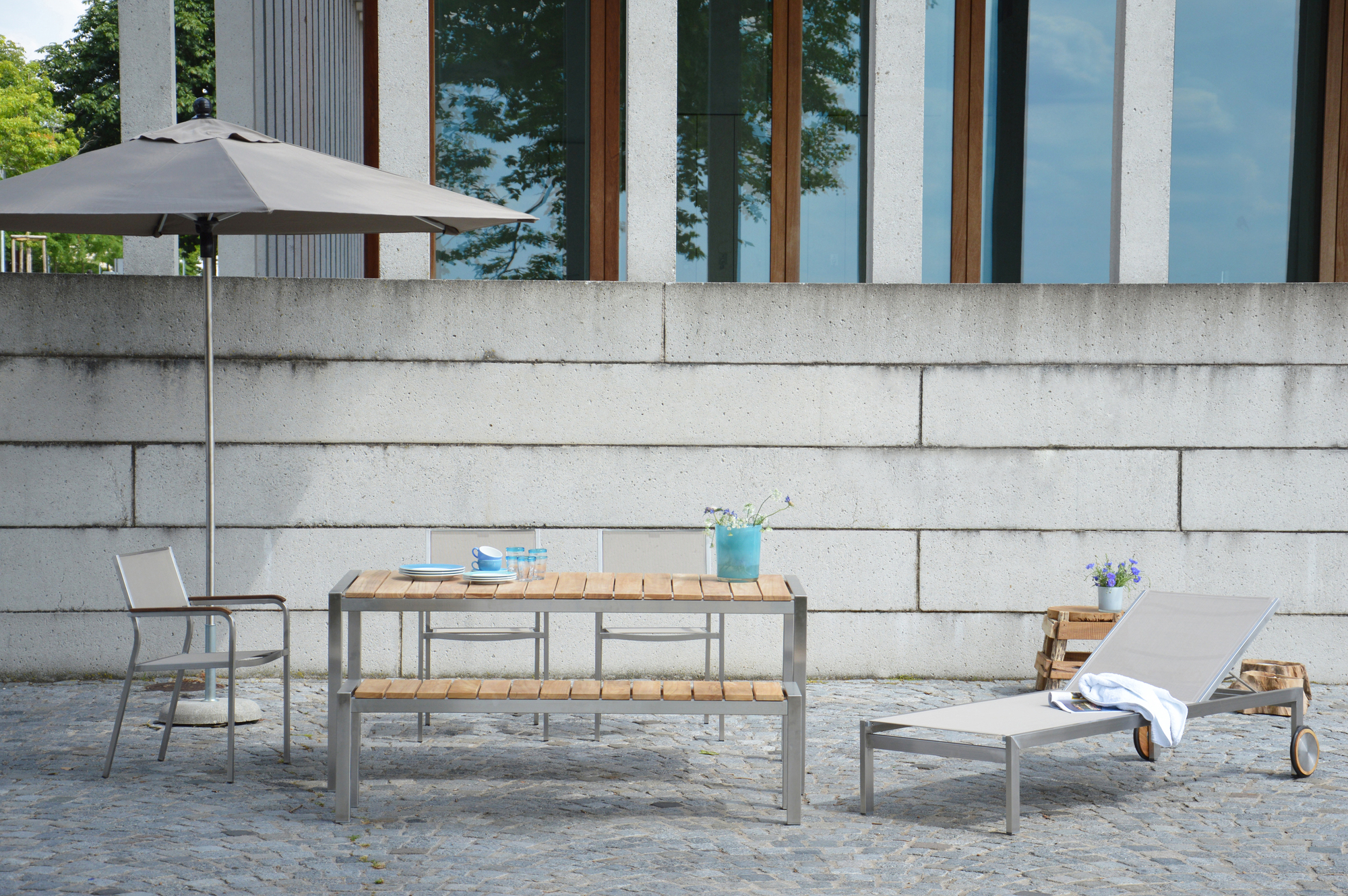 Luxury Tisch Jan Kurtz B 90 aus Holz und Metall mit Stühlen und Liege im Außenbereich.