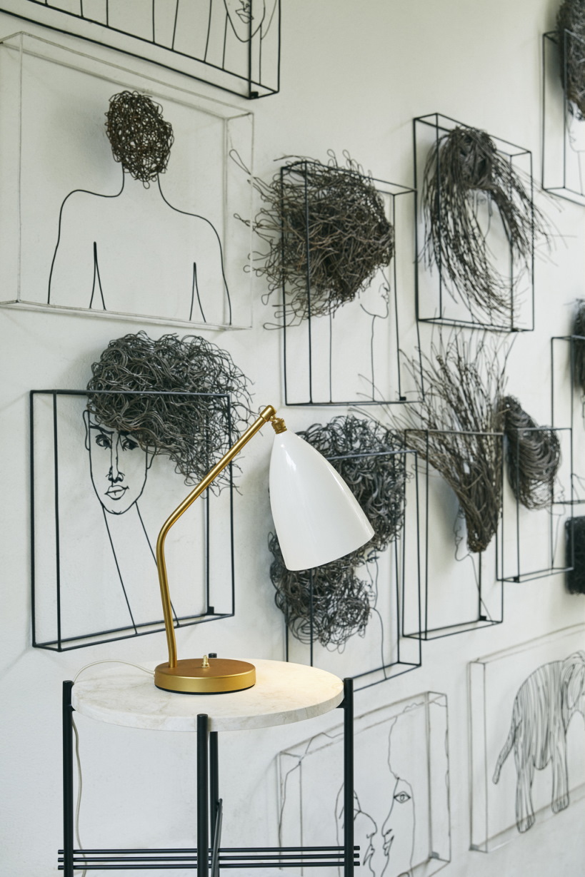 Gräshoppa Tischleuchte von Gubi, alabasterweiß glänzend, auf einem Beistelltisch vor einer Wand mit Kunst.