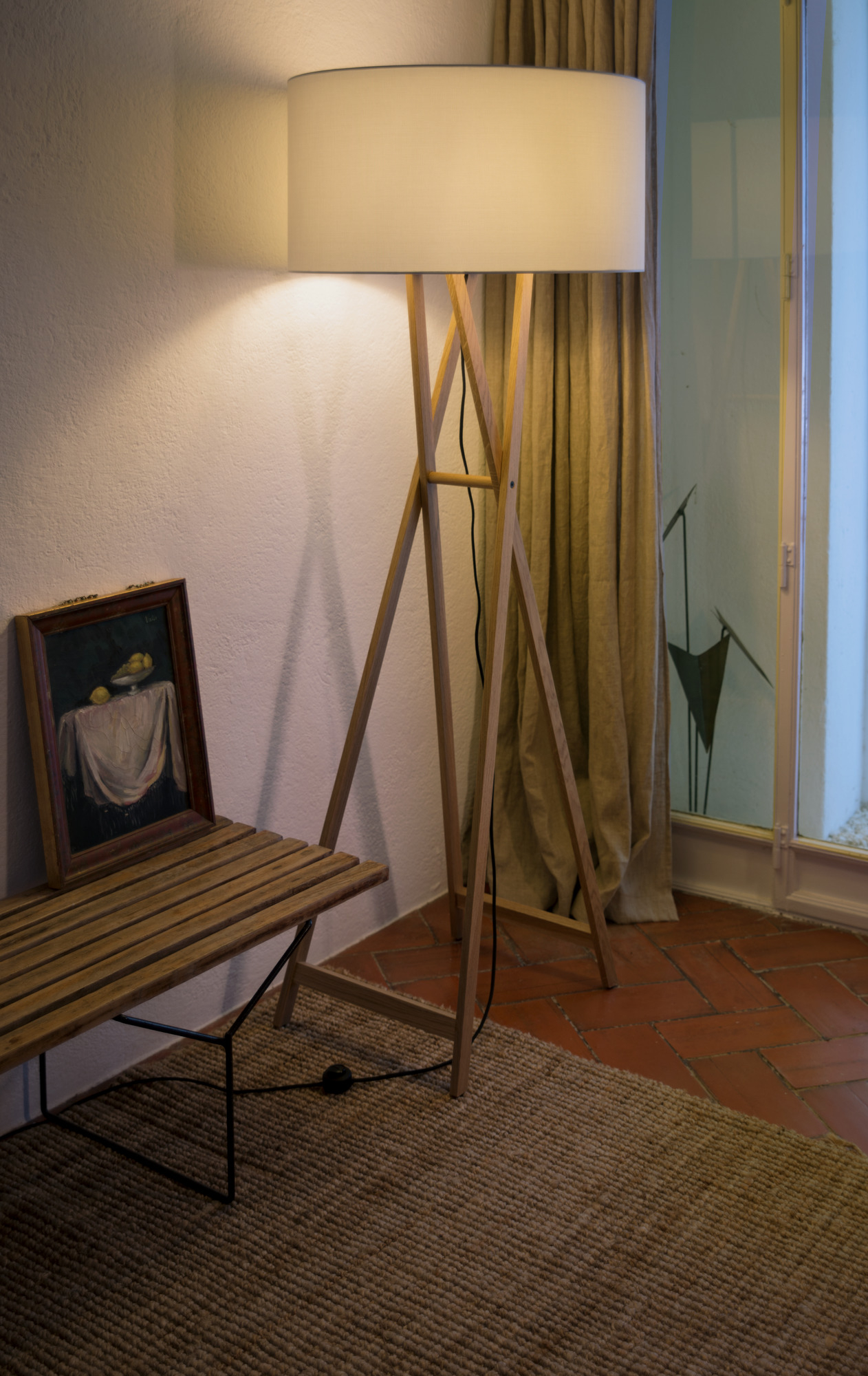 Cala Stehleuchte von Marset mit Holzgestell und hellem Lampenschirm neben Bank.