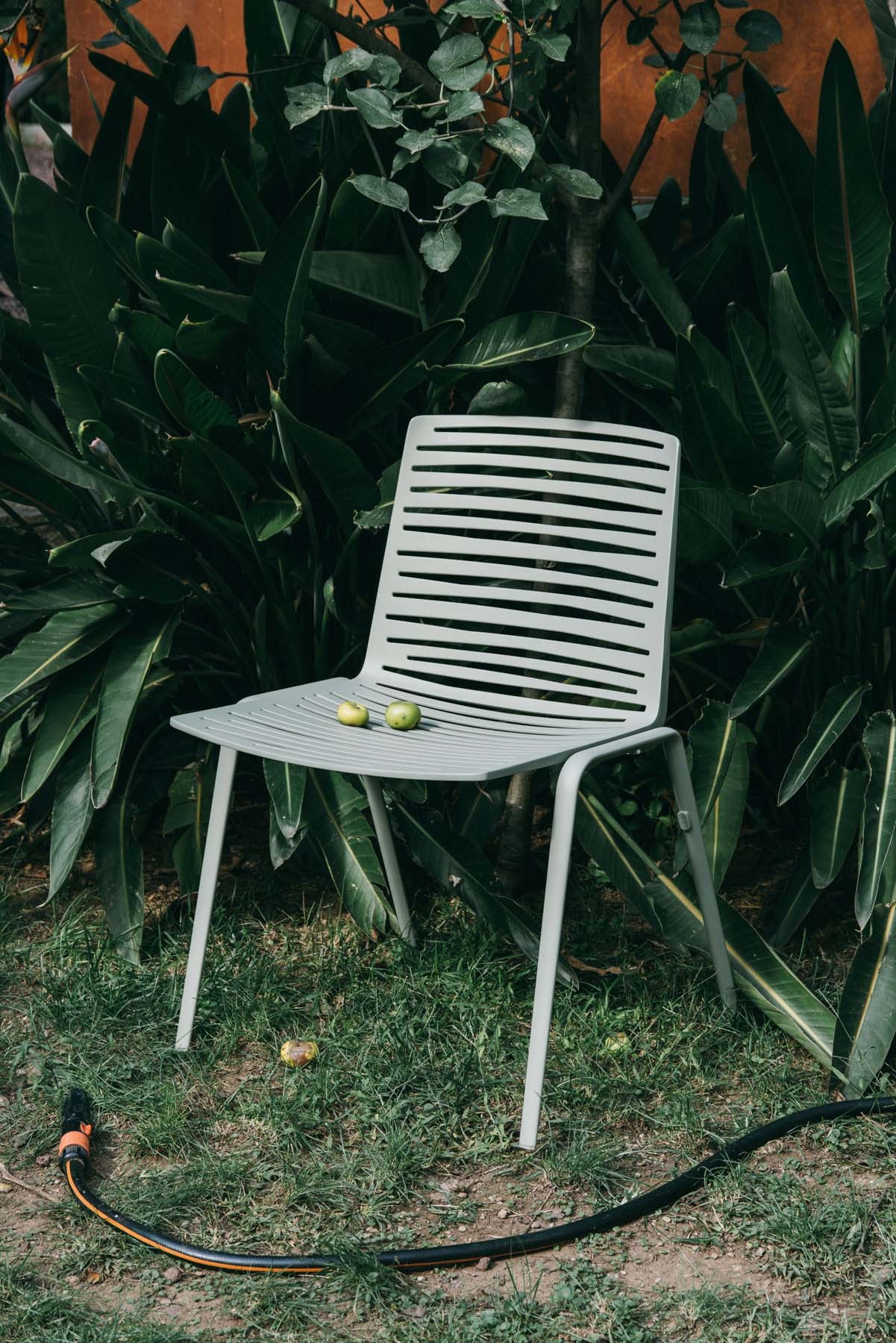 Zebra Outdoor Stuhl Fast, hellgrau, mit zwei Äpfeln auf der Sitzfläche, vor üppigem Grün.