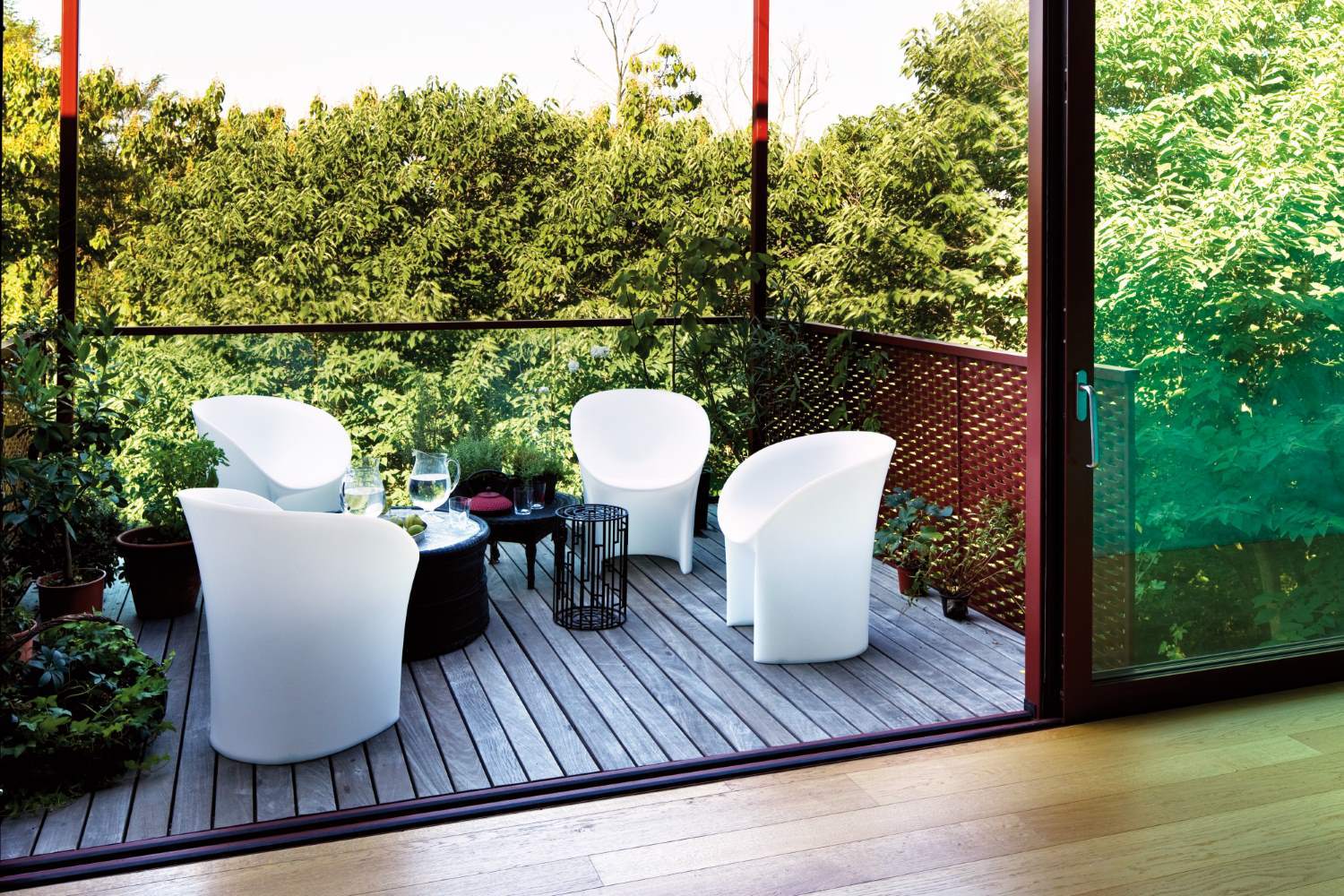 Vier weiße Moon Sessel von Moroso auf einer Holzterrasse mit Pflanzen und Tisch.