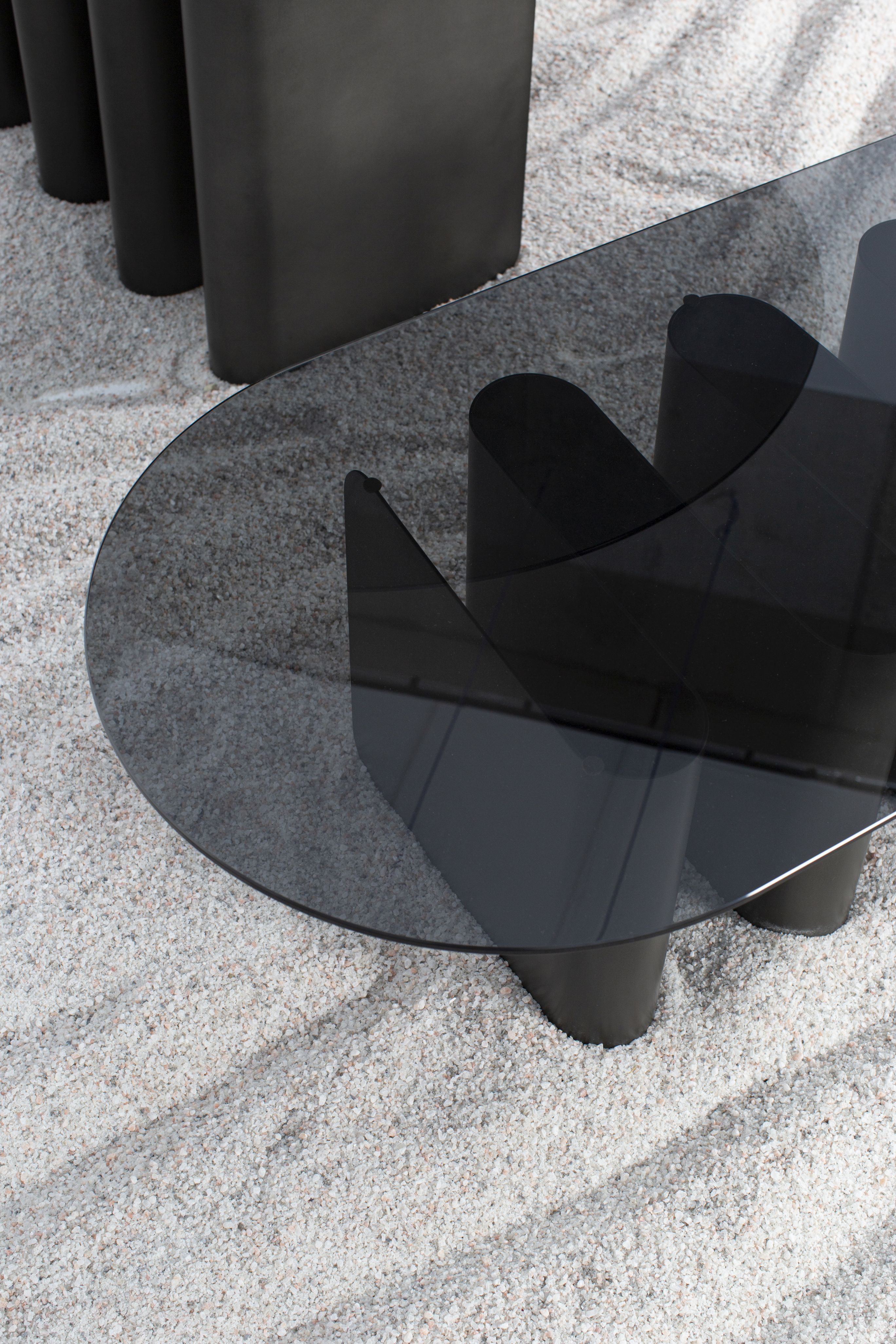 Nahaufnahme des modernen Tavolino2 Beistelltisches von Pulpo mit ovaler Glasplatte und schwarzen Beinen auf Kies.