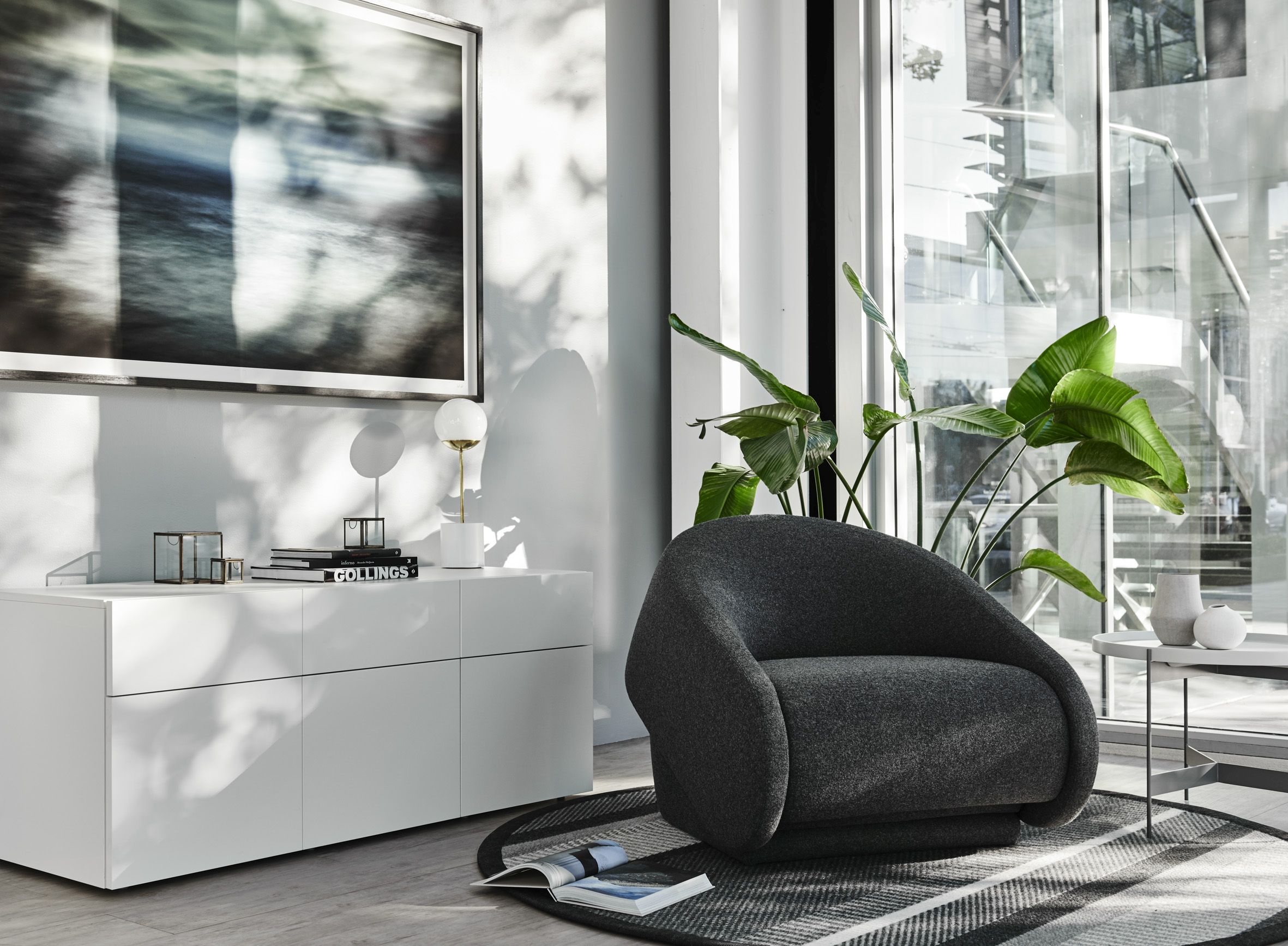 Grauer Up-lift Sessel von Prostoria im modernen Wohnzimmer mit weißem Sideboard und Fensterfront.