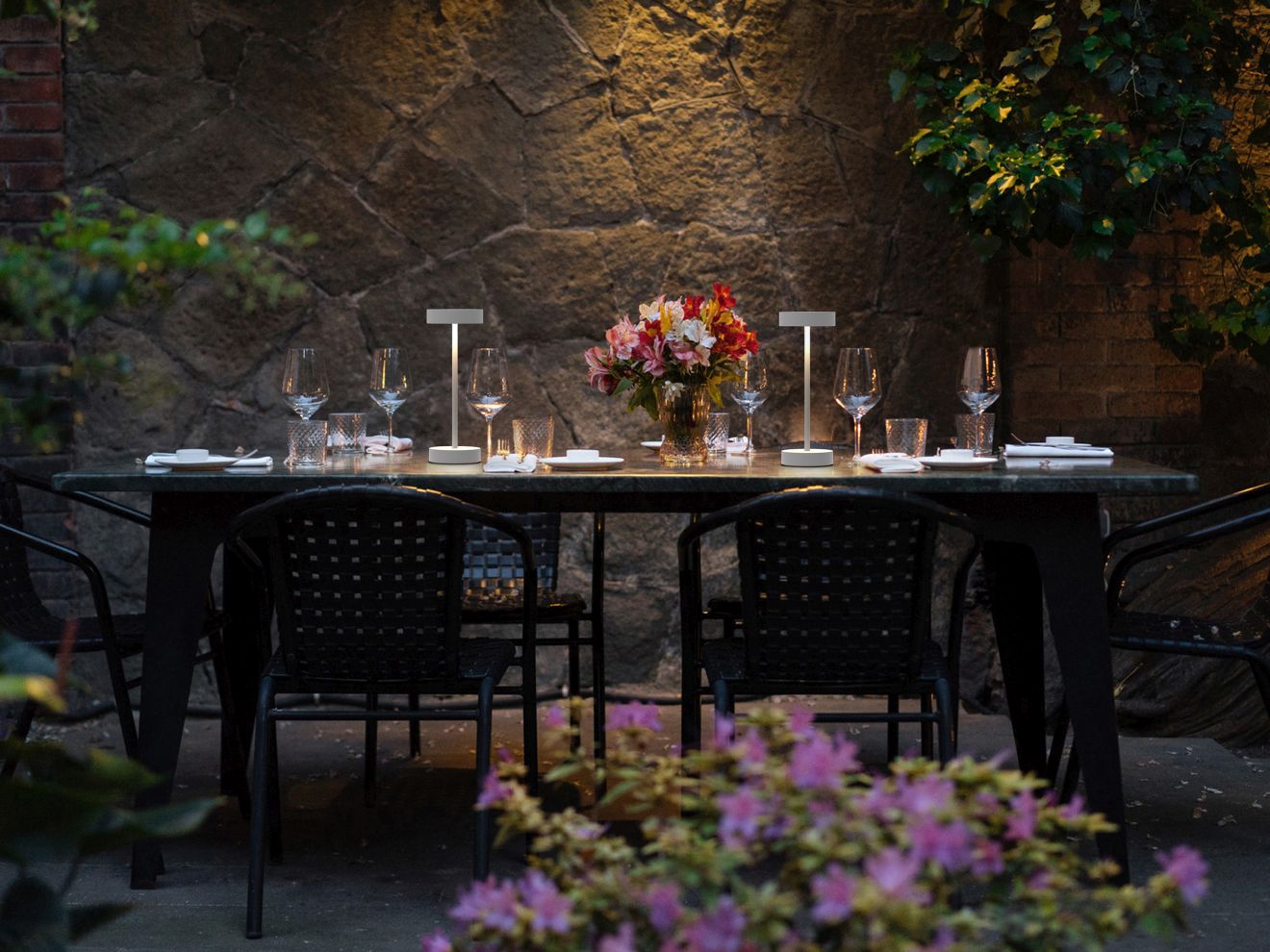 Arnold S Akkuleuchte in Weiß auf gedecktem Gartentisch, stimmungsvolle Outdoor Beleuchtung.