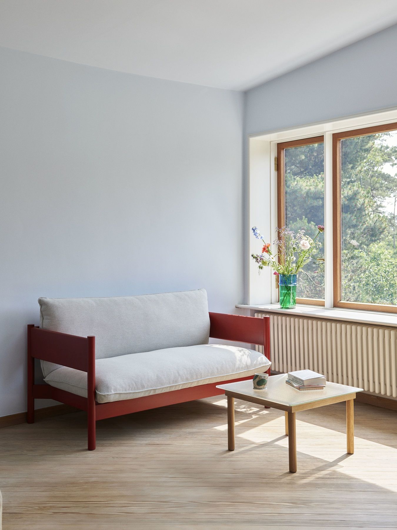 Helles Wohnzimmer mit Arbour Sofa von Hay, rotem Holzrahmen und beigen Polstern.