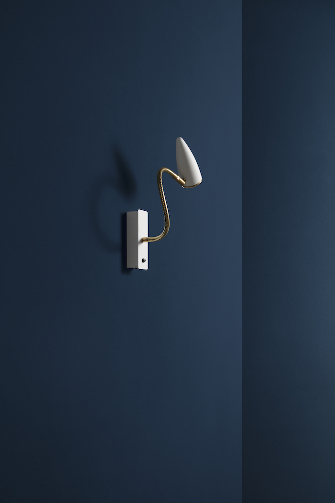 Weiße CicloItalia Wandleuchte mit flexiblem Arm und goldenen Details vor blauem Hintergrund.