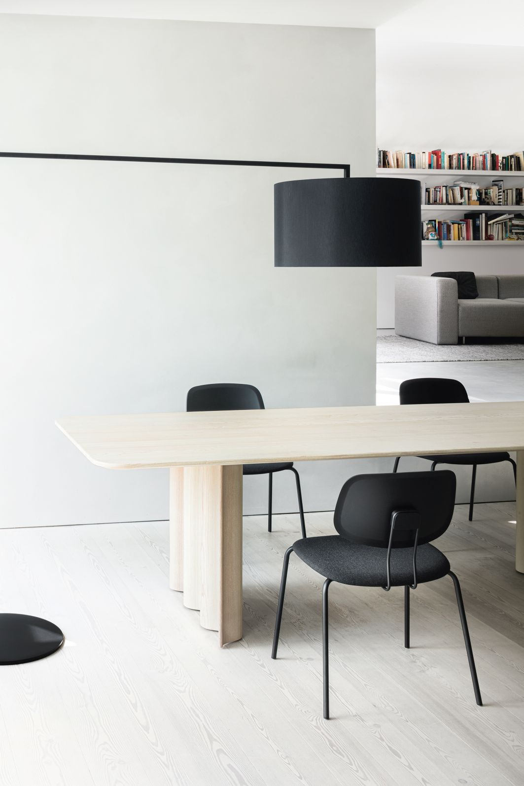 Helle Esszene mit High Noon Stehleuchte, Esstisch und schwarzen Stühlen im minimalistischen Design.