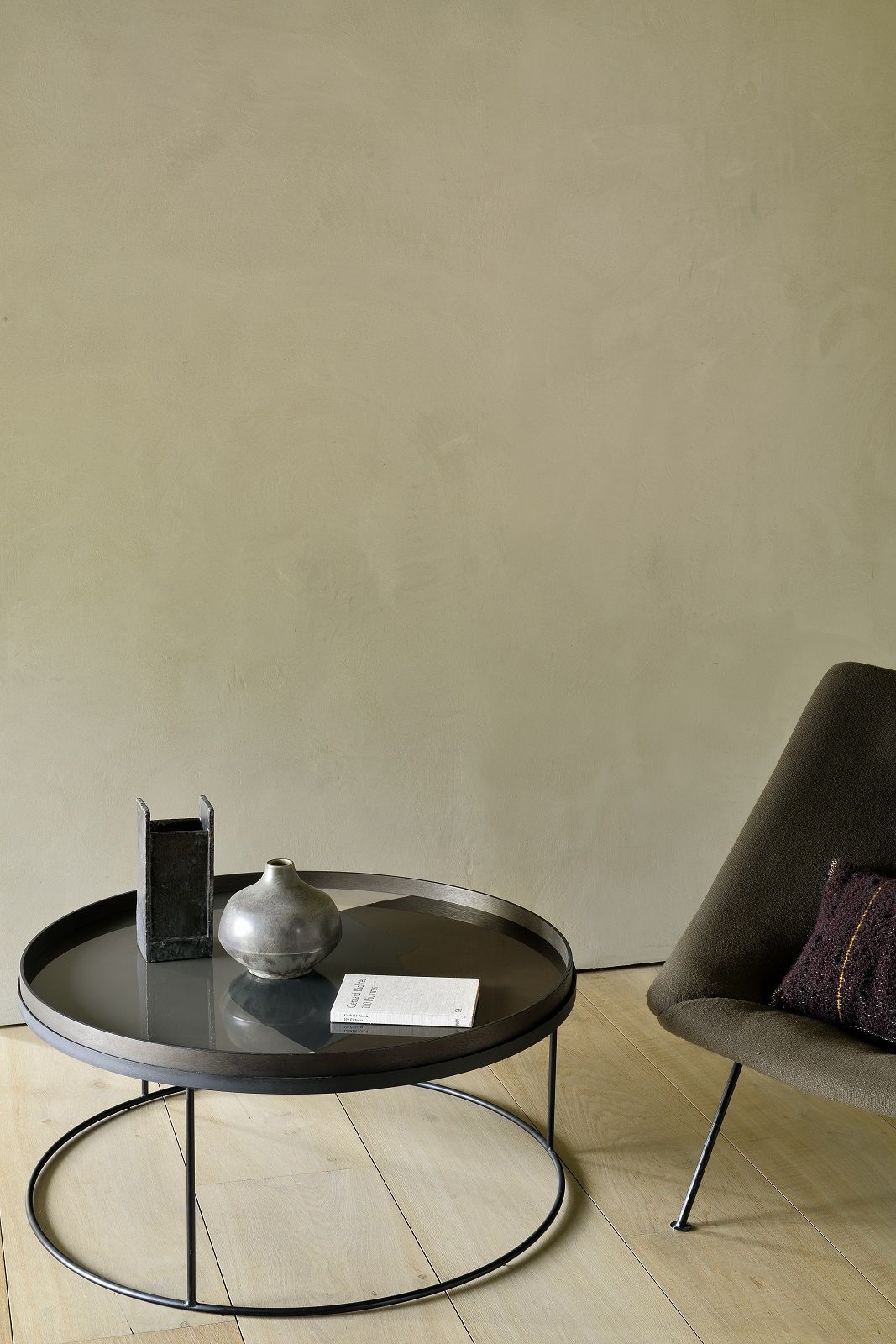 Ethnicraft Couchtisch: Runder Tabletttisch aus dunklem Holz mit Deko-Elementen und Sessel.