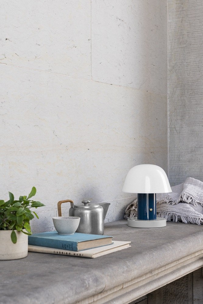 Setago Akkuleuchte Twilight & Sand von AndTradition auf Tisch mit Teekanne und Buch.