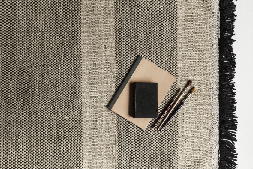 Detailaufnahme des Nanimarquina Tres Stripes Teppichs in Schwarz, 80x240cm, mit Notizbüchern und Pinseln dekoriert.