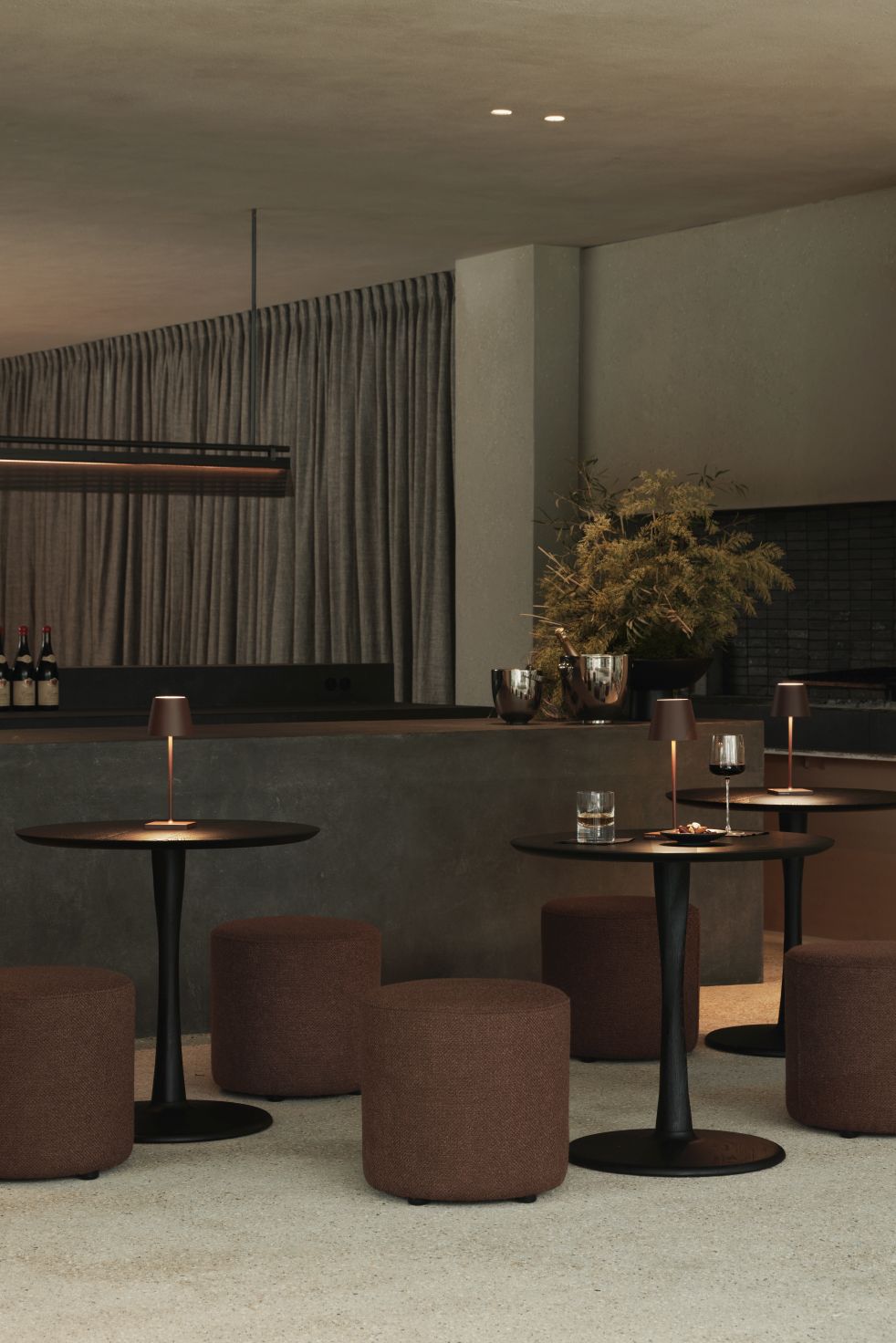 Ethnicraft Torsion Tisch niedrig, Ø90cm, Eiche schwarz, in stilvollem Ambiente mit Hockern und gedämpfter Beleuchtung.