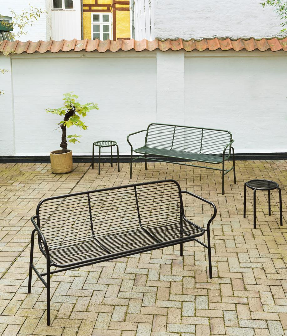 Normann Copenhagen Vig Dining Bench Outdoor: Schwarze und grüne Metall Gartenbank und Hocker auf Pflastersteinen.
