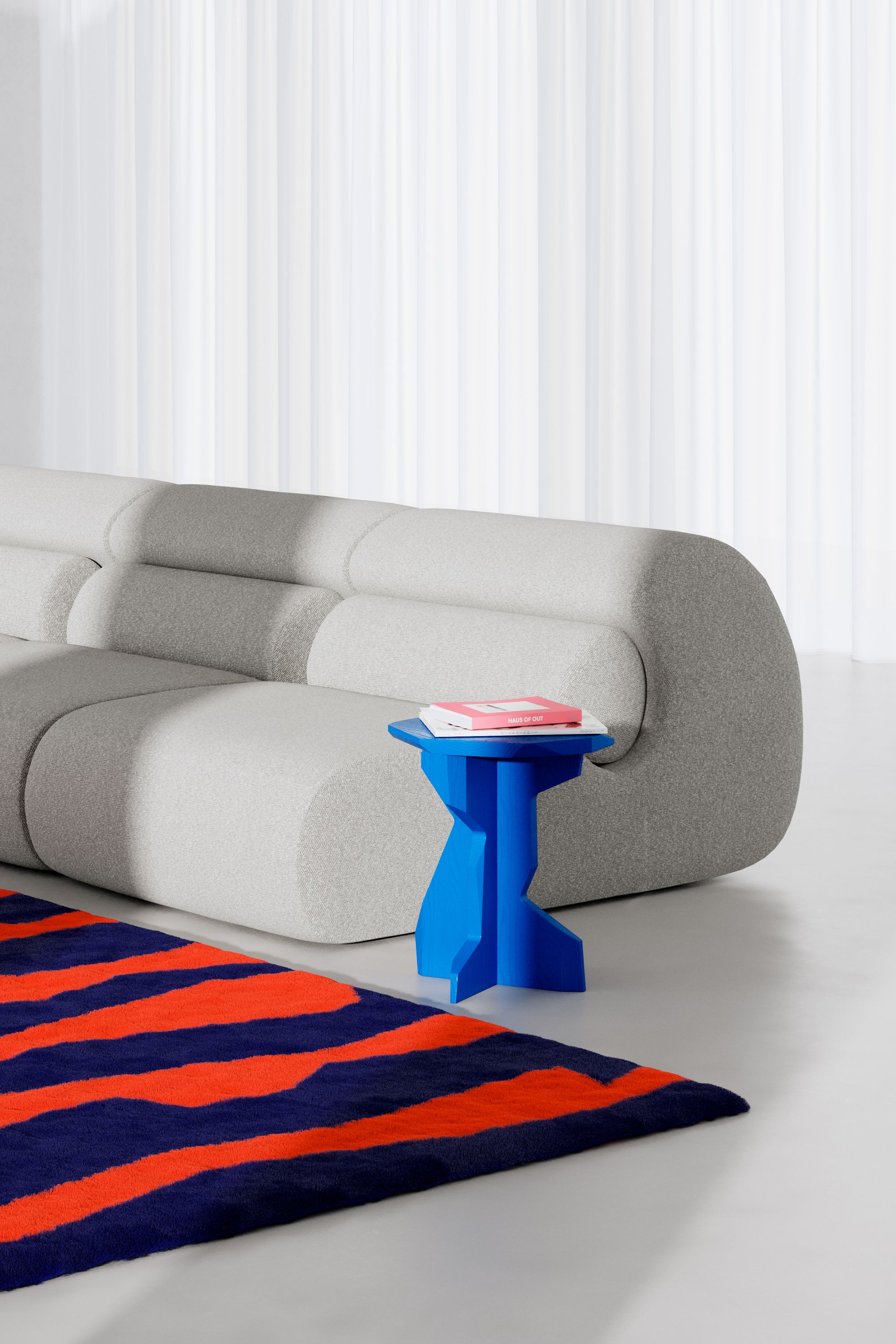 Blauer FELS Hocker aus Esche neben grauem Sofa und Teppich mit Streifenmuster.