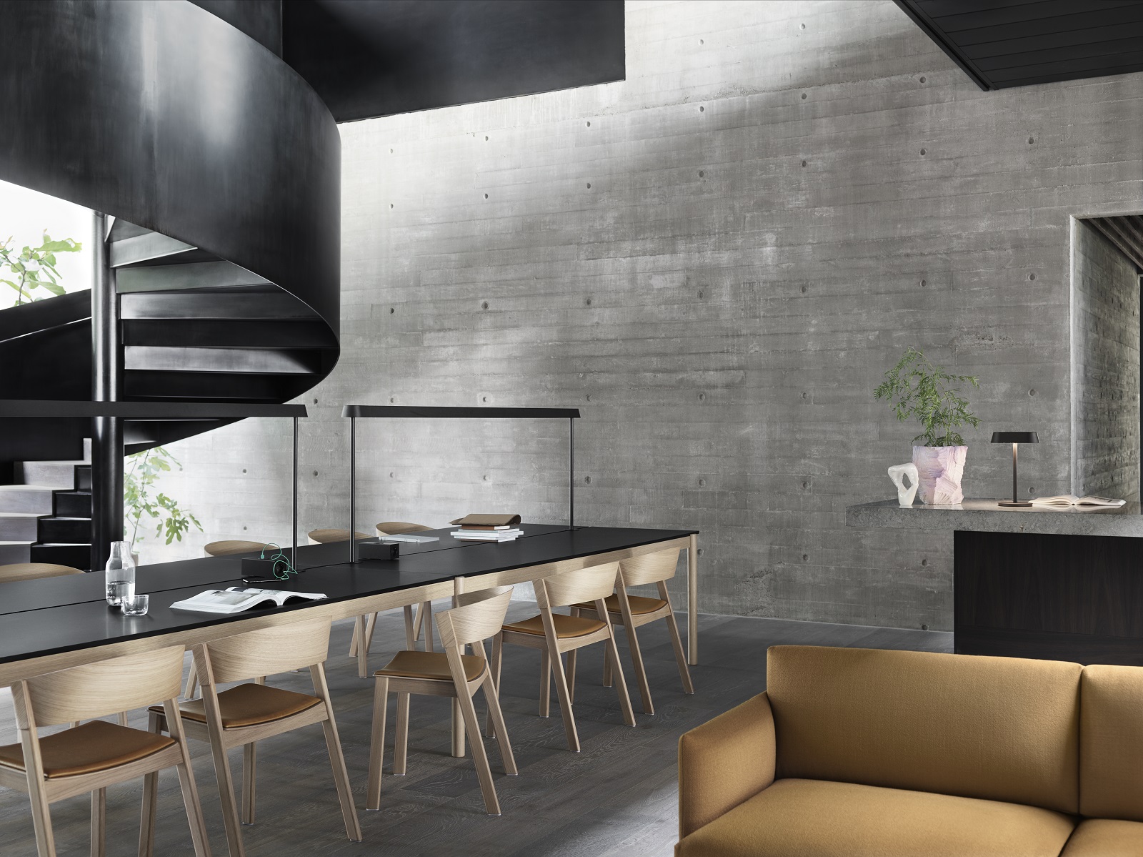Innenraum mit Muuto Outline Studio Sofa, Esstisch mit Stühlen und Wendeltreppe vor Betonwand.