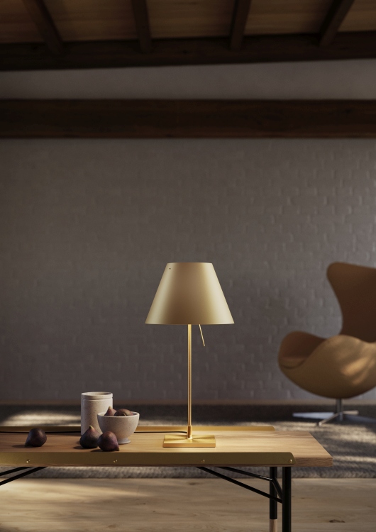 Costanzina Tischleuchte aus Messing von Luceplan: Elegante, goldfarbene Lampe auf einem Holztisch mit Feigen.