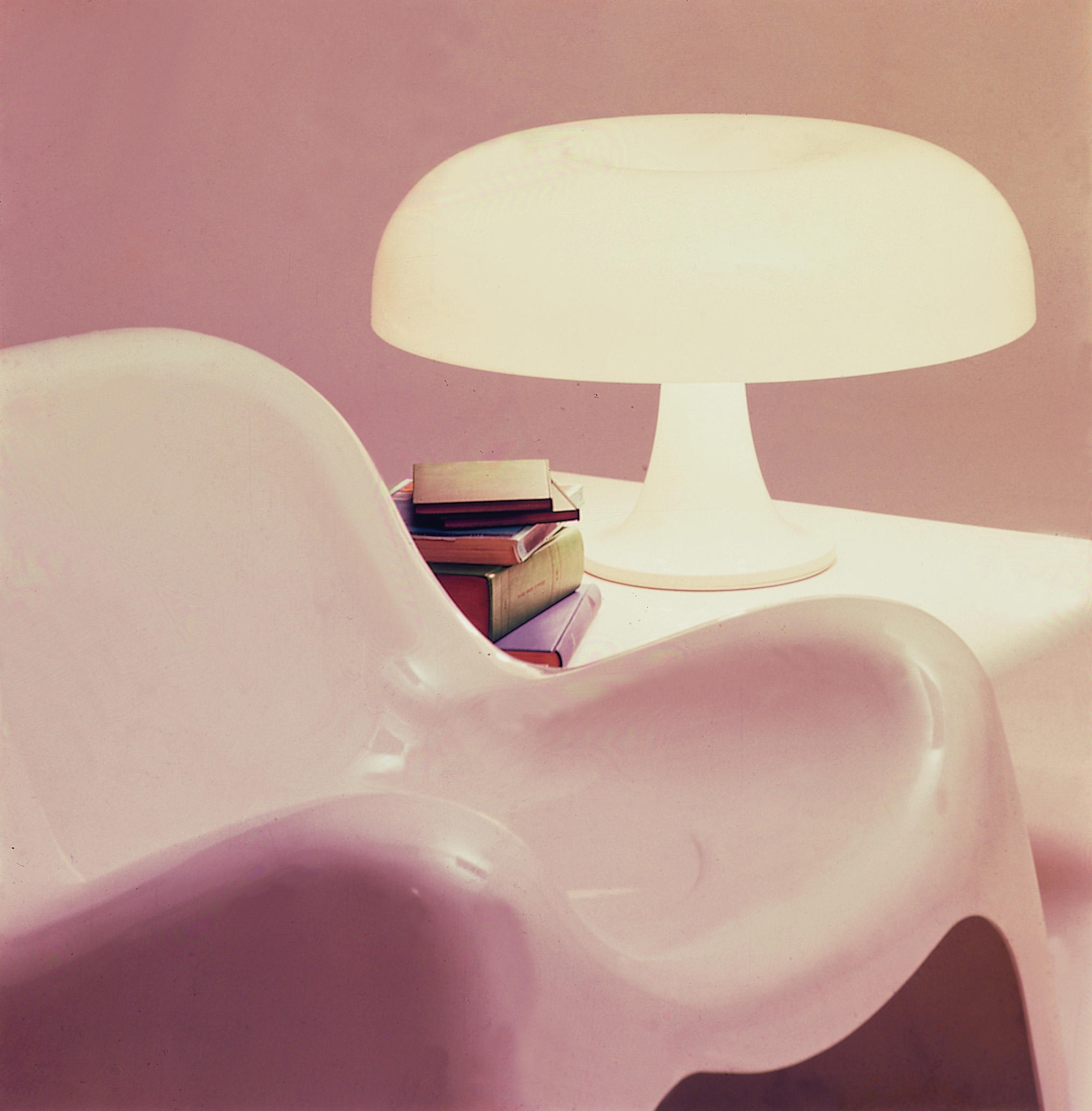 Nesso Tischleuchte von Artemide neben einem Stapel Bücher auf einem weißen Tisch.