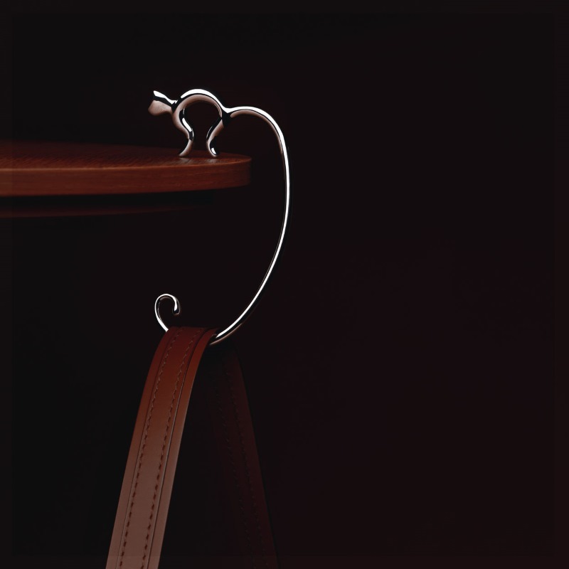 Alessi Minou Taschenhaken am Tisch mit brauner Handtasche, praktischer Taschenhalter für unterwegs.