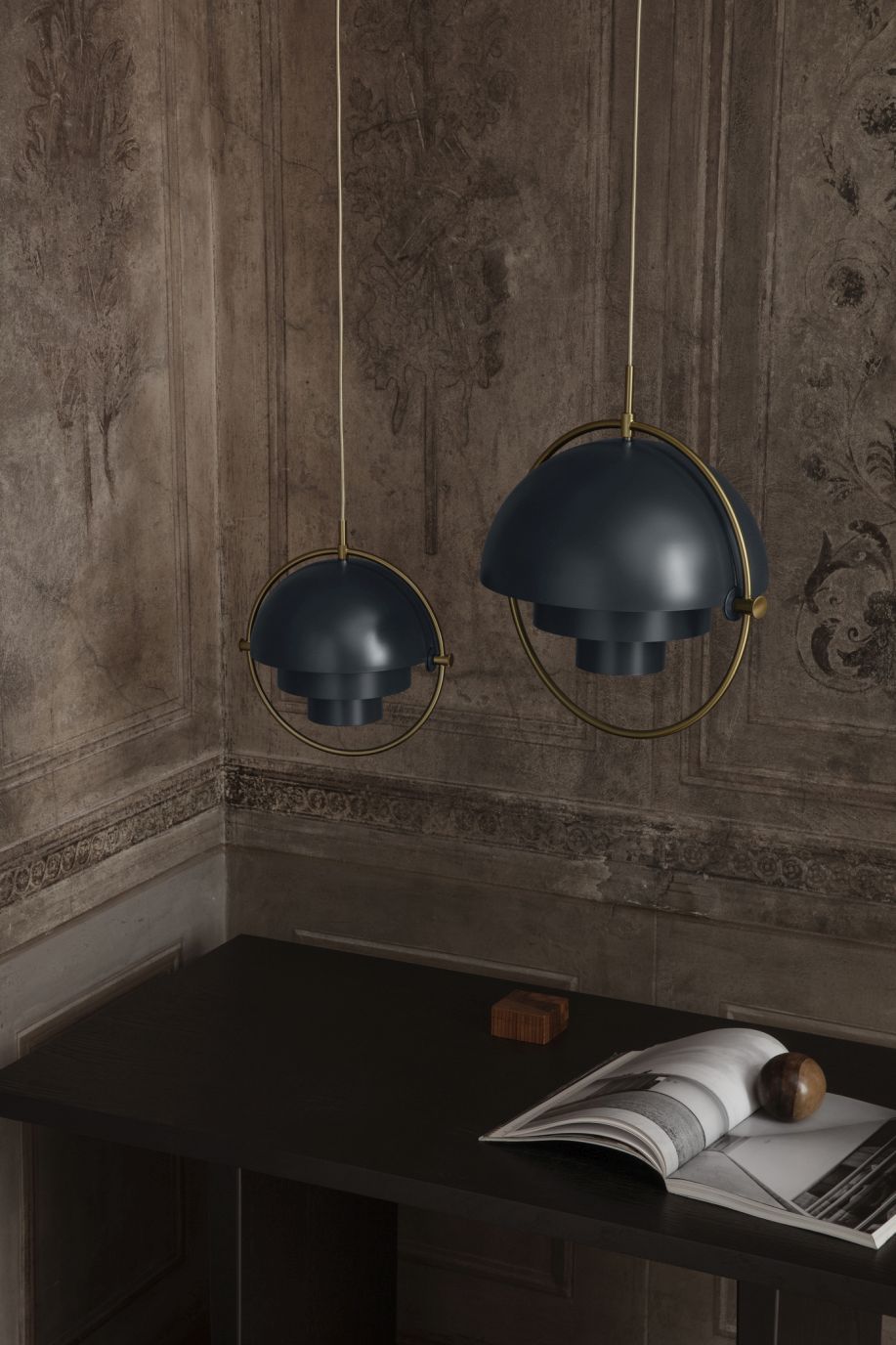 Zwei graue Gubi Multi-Lite Pendelleuchten mit Chrom-Details über einem dunklen Tisch.