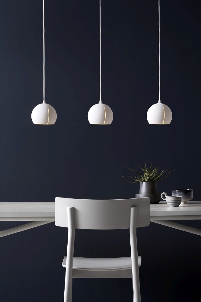 Drei runde, weiße Gap Pendelleuchten von Woud über einem Esstisch mit Stuhl.