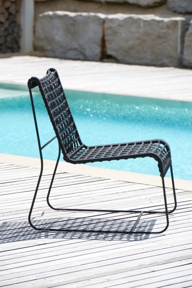 Schwarzer Jan Kurtz In/Out Lounge Sessel Outdoor aus Kordel vor Pool auf Holzdeck.