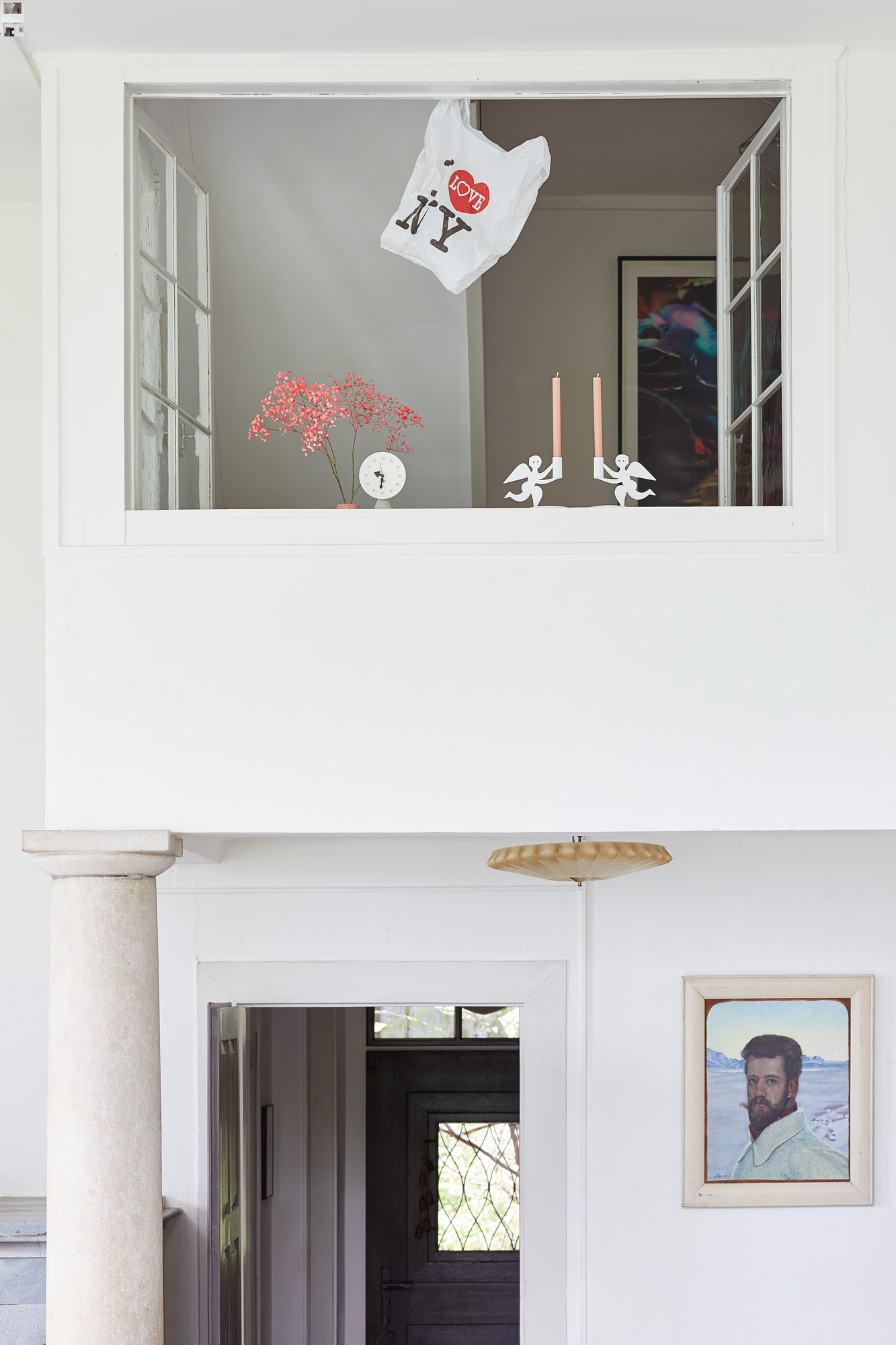 Innenaufnahme mit Vitra Tischuhr auf Fensterbank, neben Blumen, Kerzen und "I Love NY" Tüte.