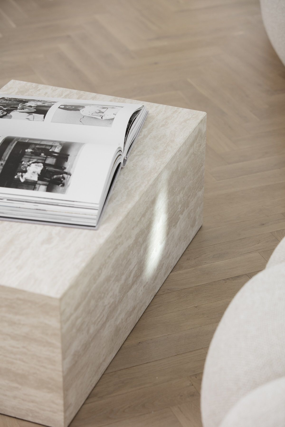Cubism Table von NORR11: Großer, beiger Couchtisch aus Travertin mit Buch auf Parkettboden.