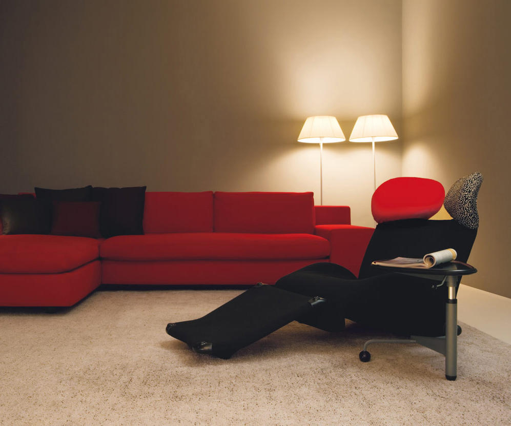 Anthrazitfarbener 111 Wink Sessel von Cassina mit rotem Sofa und Stehlampen im Hintergrund. Designermöbel für Wohnzimmer.