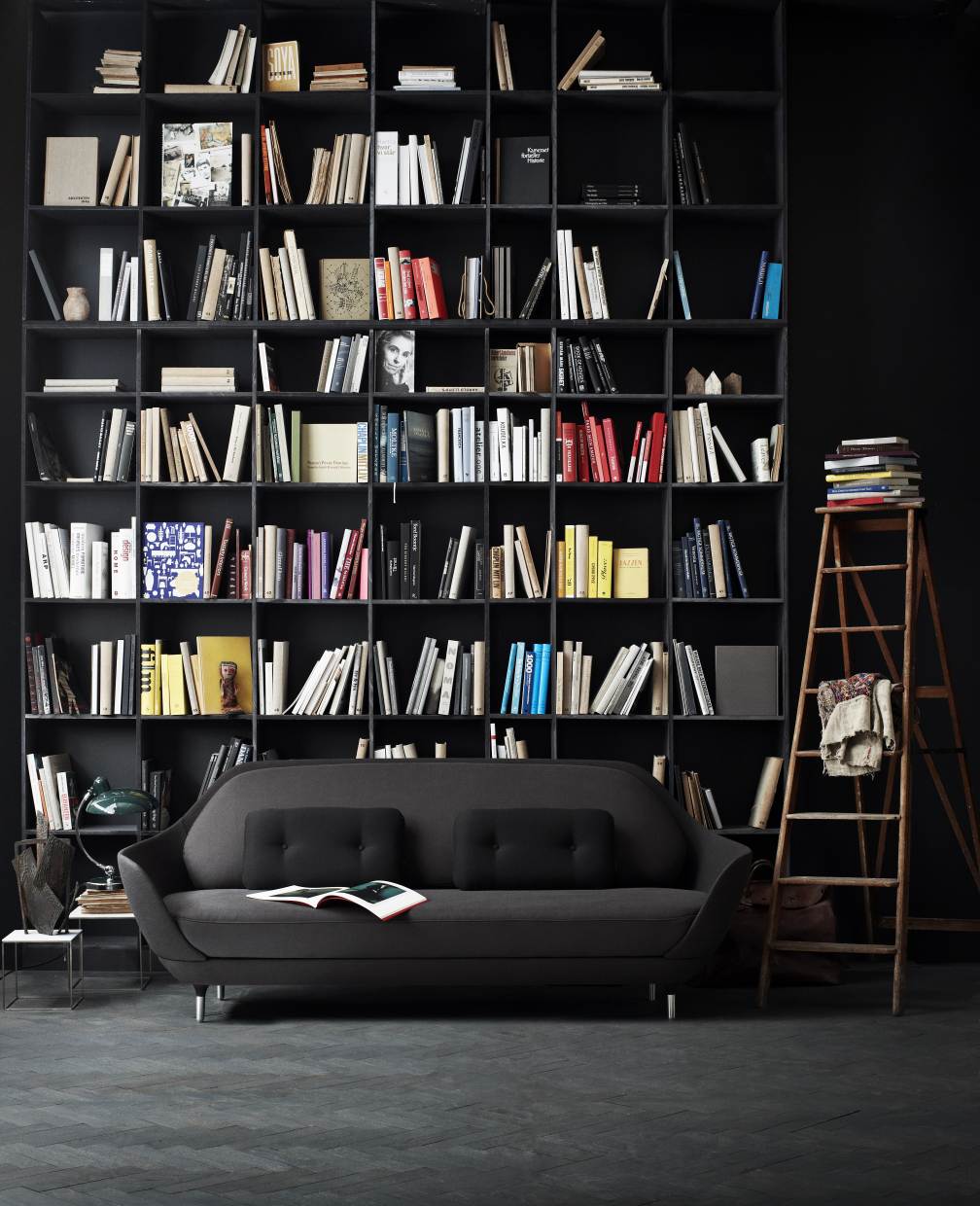 Graues Favn Sofa von Fritz Hansen vor einem großen Bücherregal in dunklem Raum.