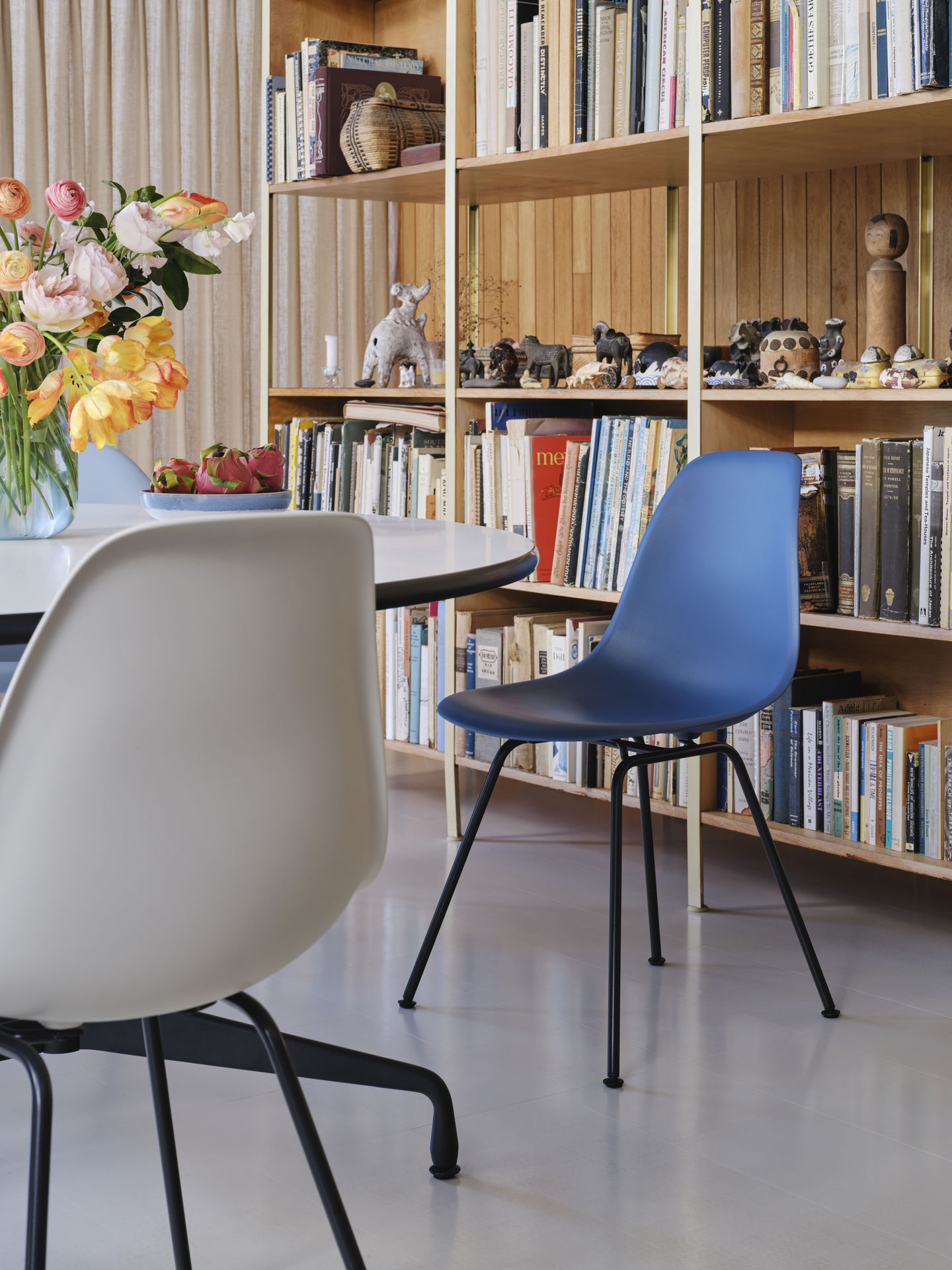 Blauer Eames Plastic Side Chair DSX von Vitra am Esstisch vor Bücherregal.
