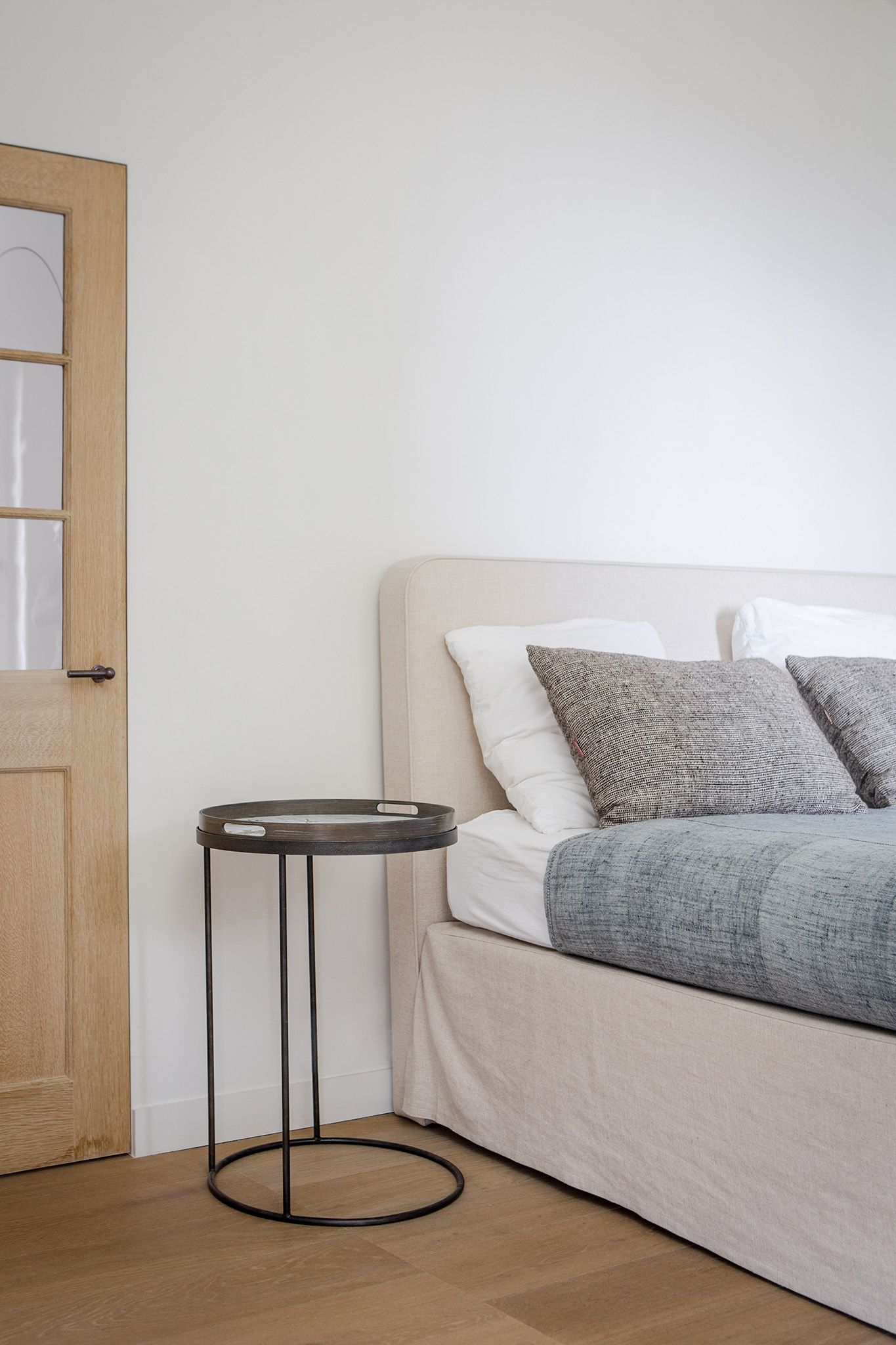 Schwarzer Ethnicraft Beistelltisch aus Holz neben einem Bett in einem hellen Schlafzimmer.