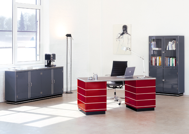 TB229 Classic Line Schreibtisch von Müller Möbelfabrikation in Rot, mit Büromöbeln und Accessoires in einem hellen Raum.
