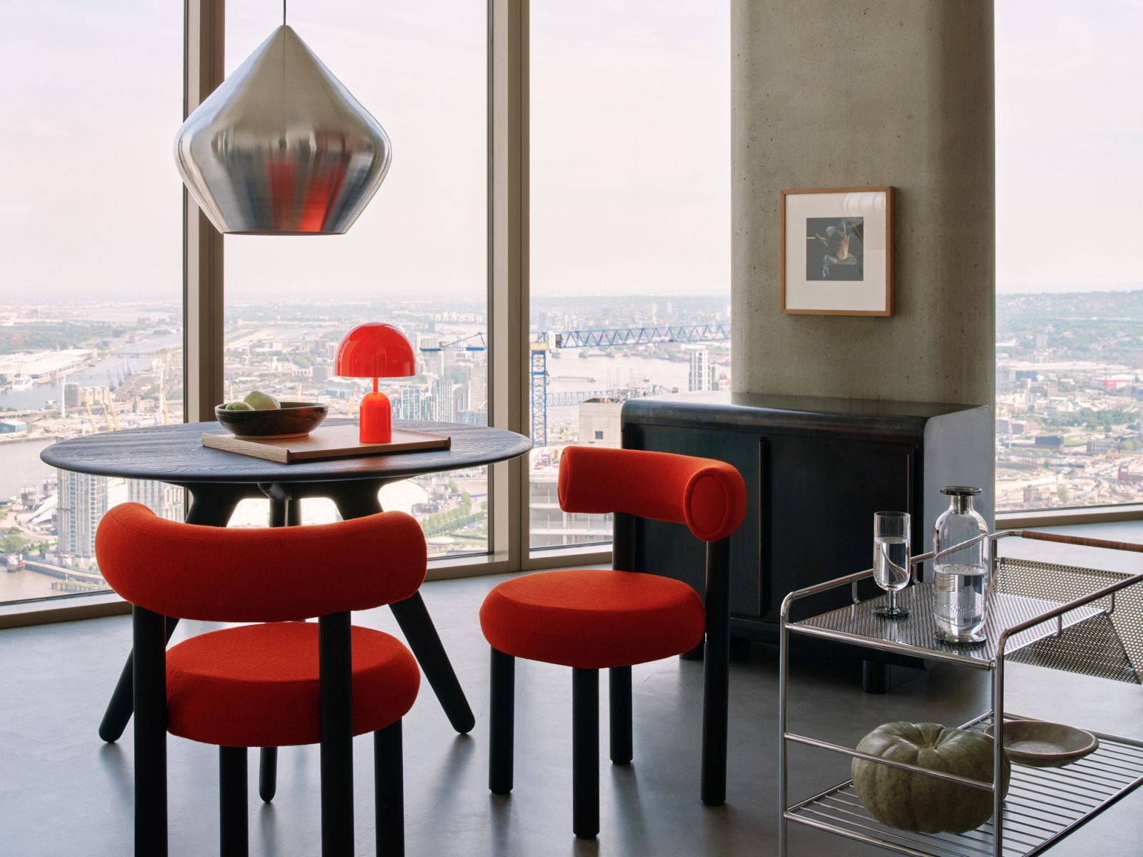 Moderne Esszene mit Tom Dixon Unbeaten Stout Pendelleuchte über einem runden Esstisch mit roten Stühlen.