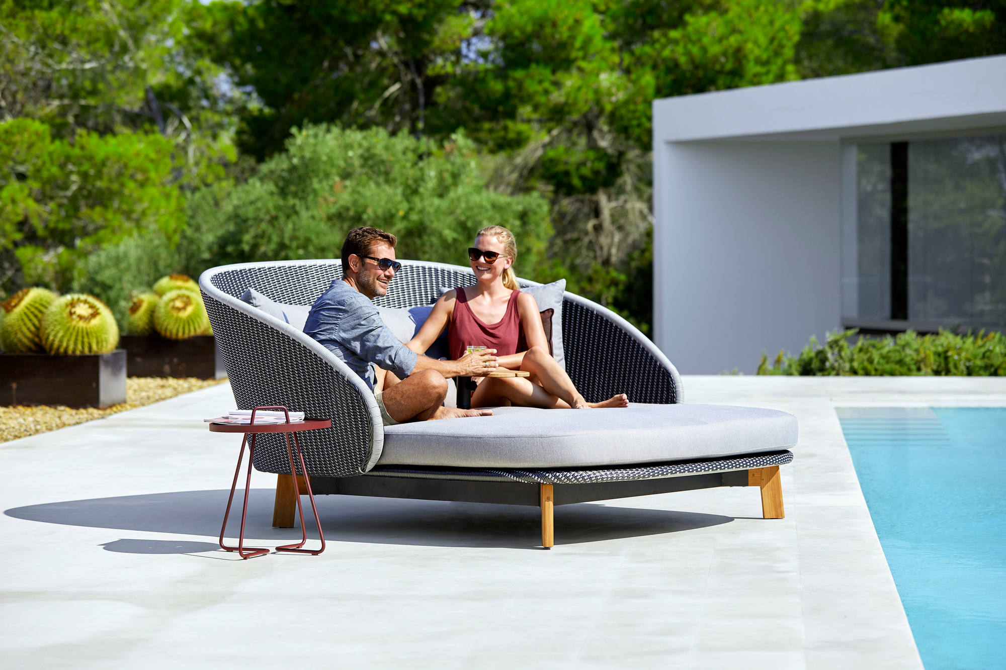 Paar entspannt auf Cane-Line Peacock Outdoor Liege mit Tisch und Kissen am Pool.