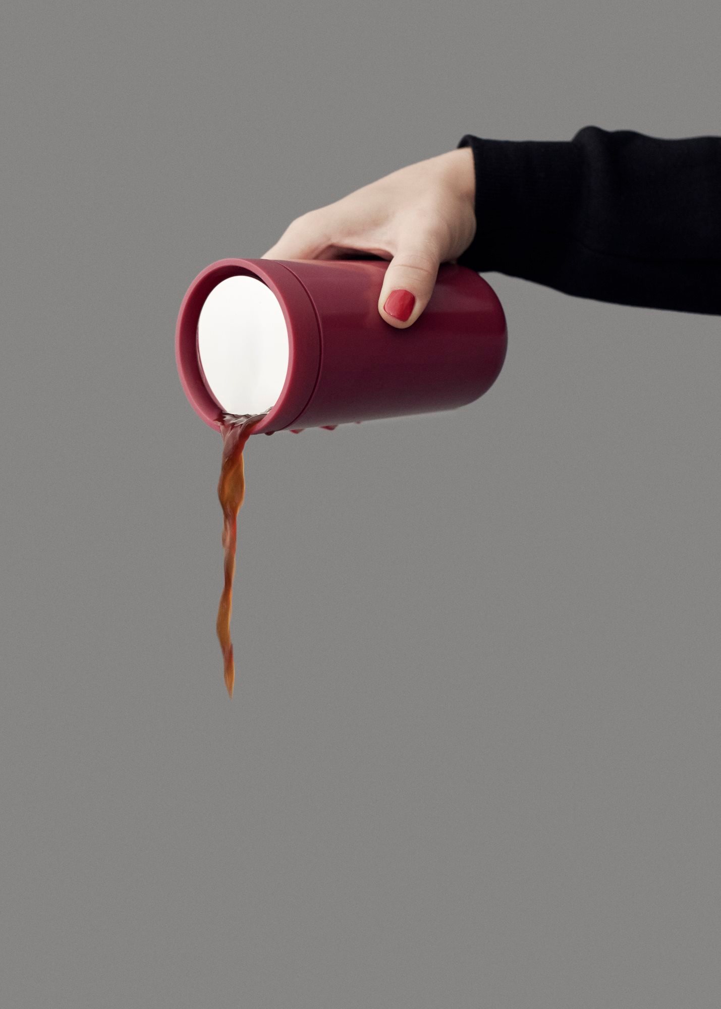 Nahaufnahme einer Hand, die einen roten Stelton To Go Click Thermobecher hält und Kaffee ausgießt.