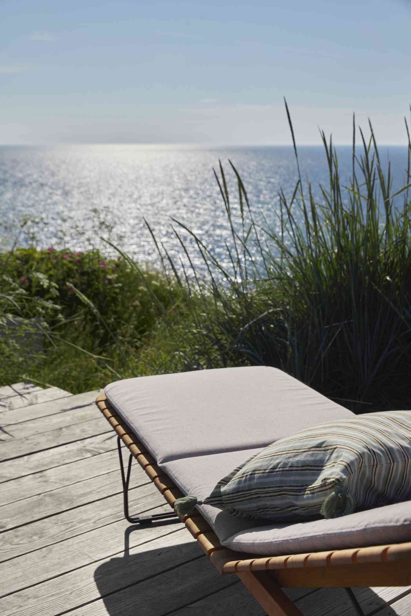 Molo Outdoor Cushion Kissen für Houe Sonnenliege auf Holzterrasse mit Meerblick. Gartenmöbel für Entspannung.