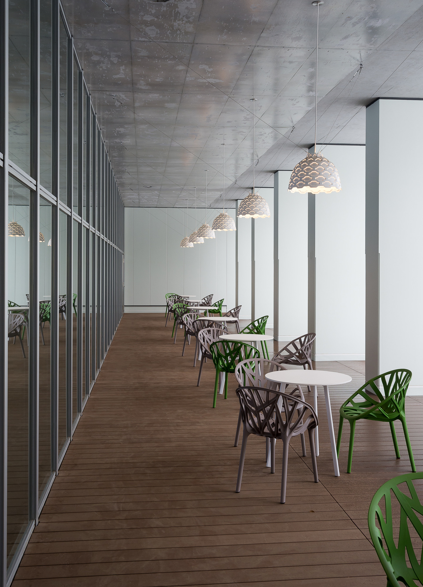 Reihe von LC Shutters Hängeleuchten von Louis Poulsen über Tischen und Stühlen in einem Raum.