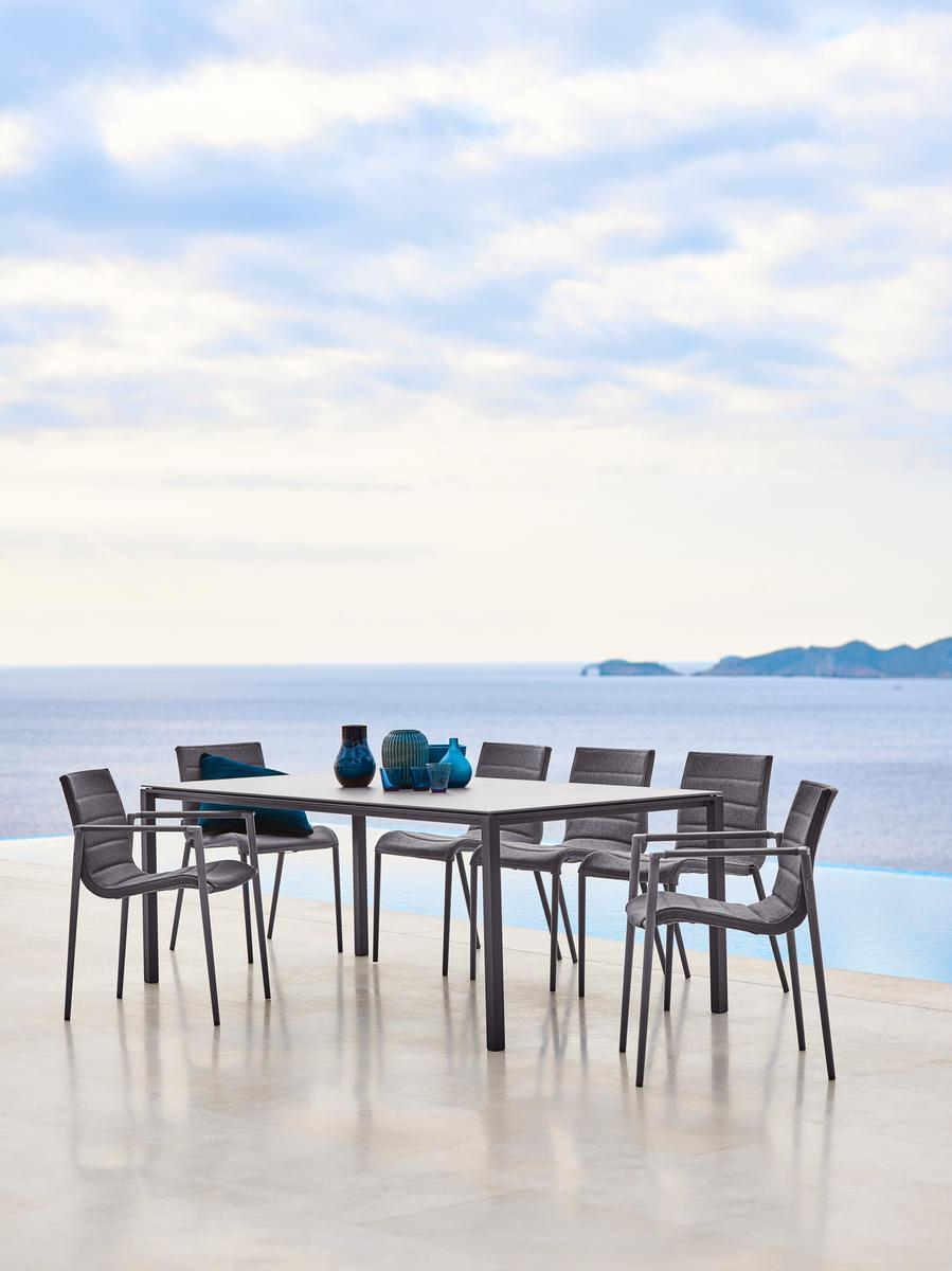 Cane-Line Core Outdoor Stuhl mit Armlehne an Esstisch mit Meerblick. Gartenmöbel für Terrasse.