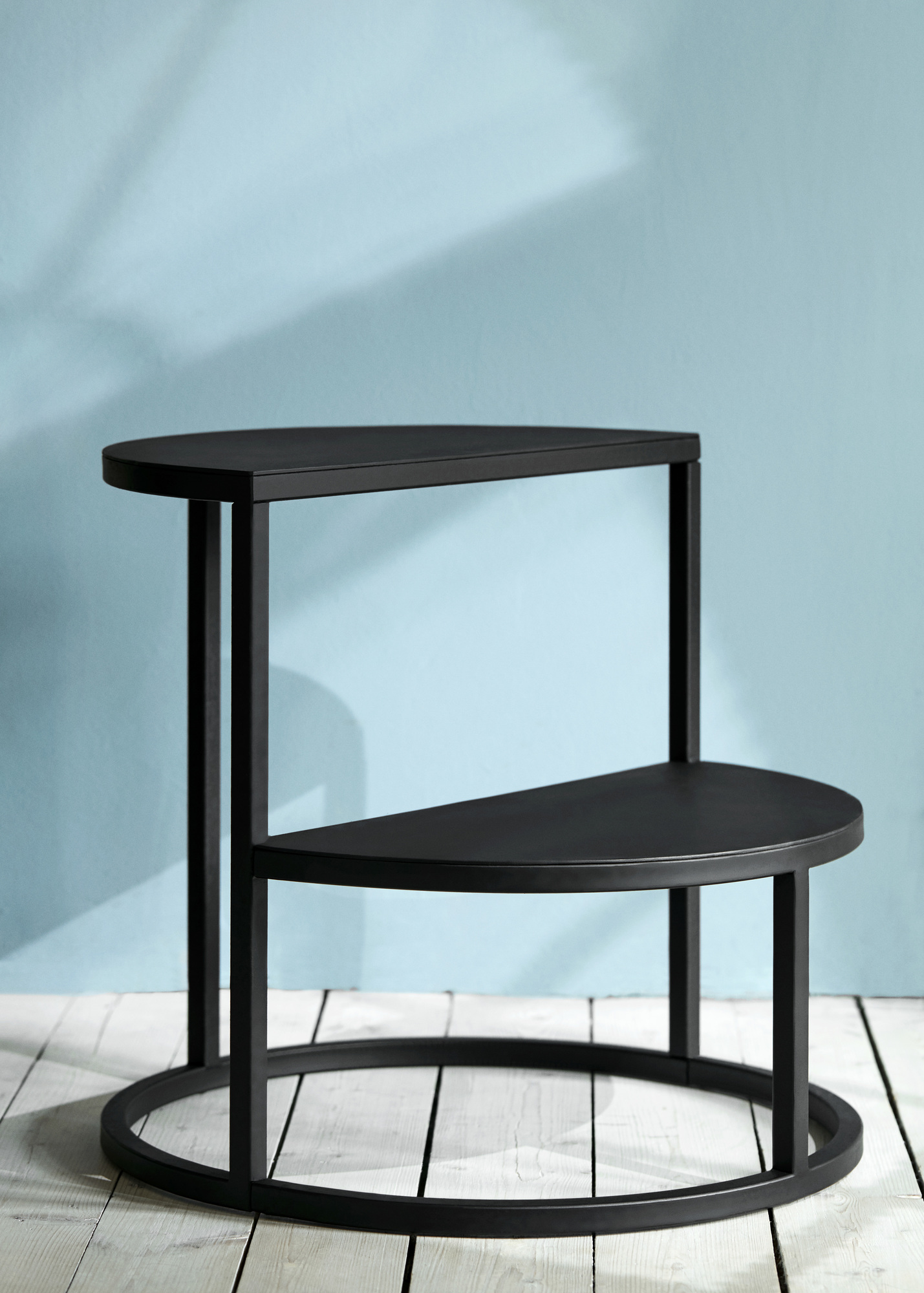 Schwarzer Dais Stufenhocker mit zwei Ablageflächen und Metallgestell auf hellem Holzboden. Dekorative Trittstufe.