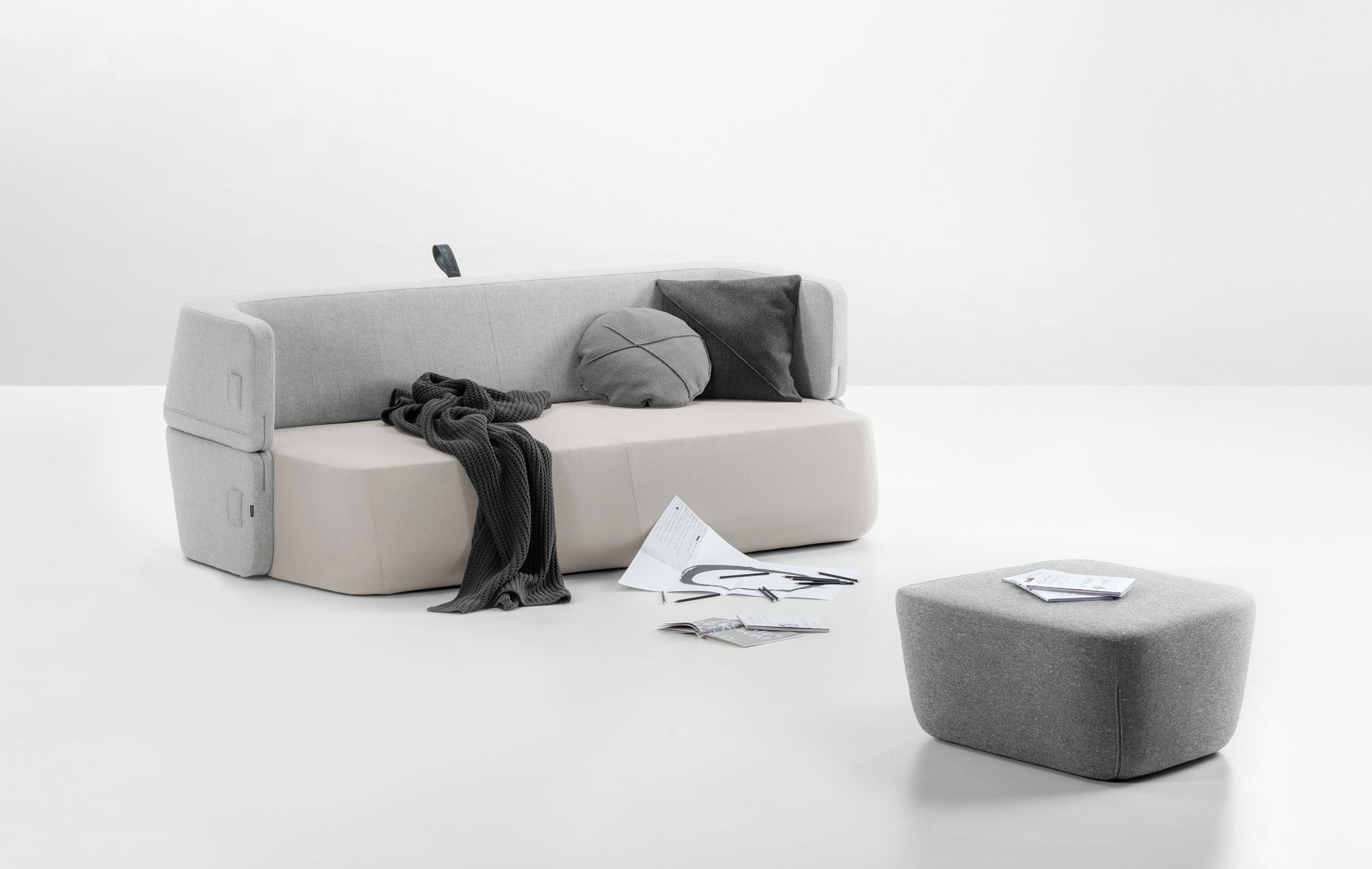 Graues Revolve Schlafsofa von Prostoria mit Kissen und Hocker auf weißem Hintergrund.