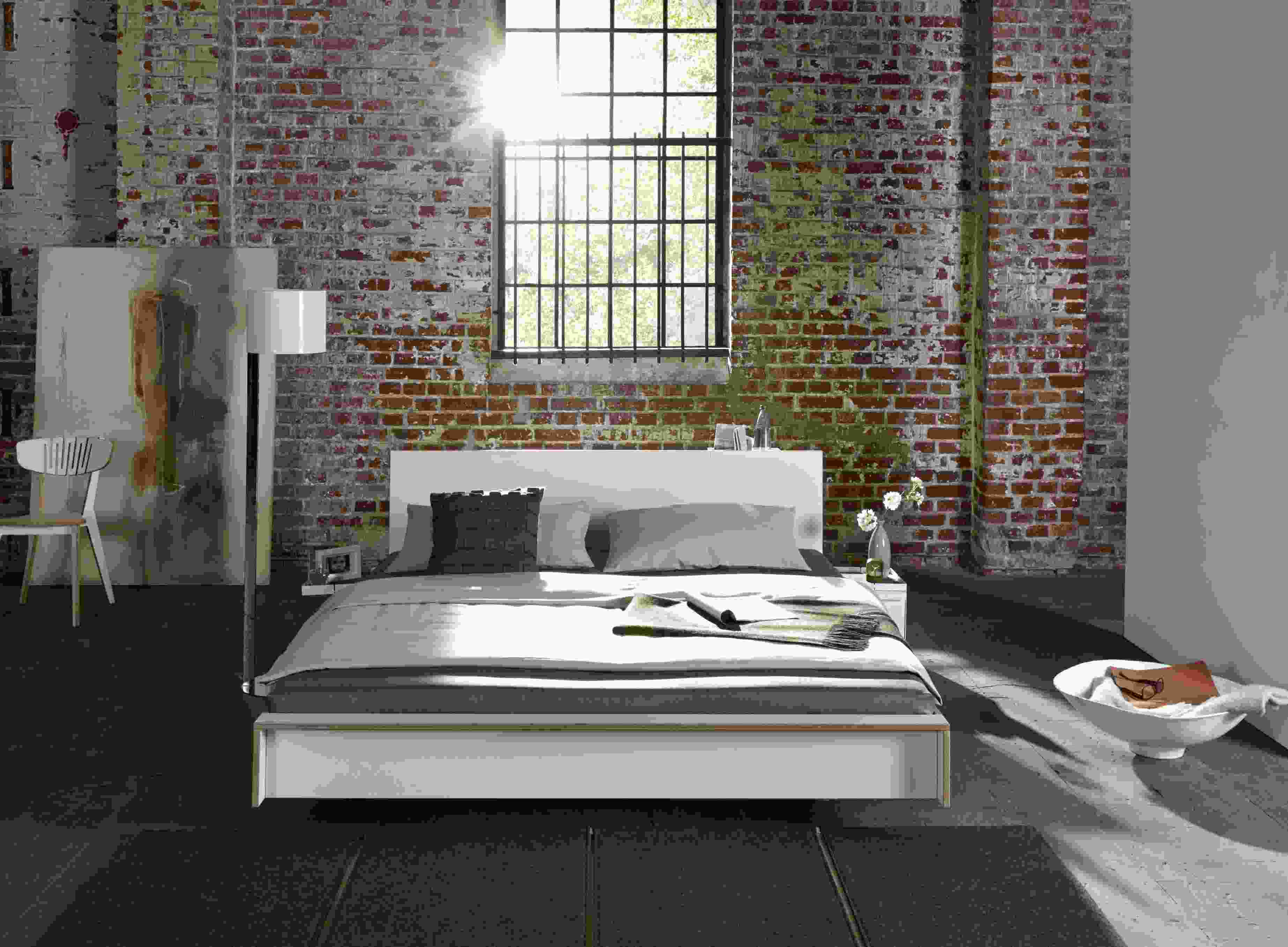 Helles Schlafzimmer mit weißem Flai Bett von Müller Möbelwerkstätten und Backsteinwand.