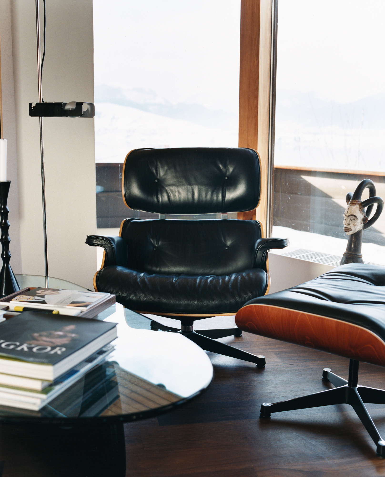 Nussbaum Couchtisch mit Glasplatte, Bücherstapel und schwarzem Ledersessel im modernen Wohnzimmer.